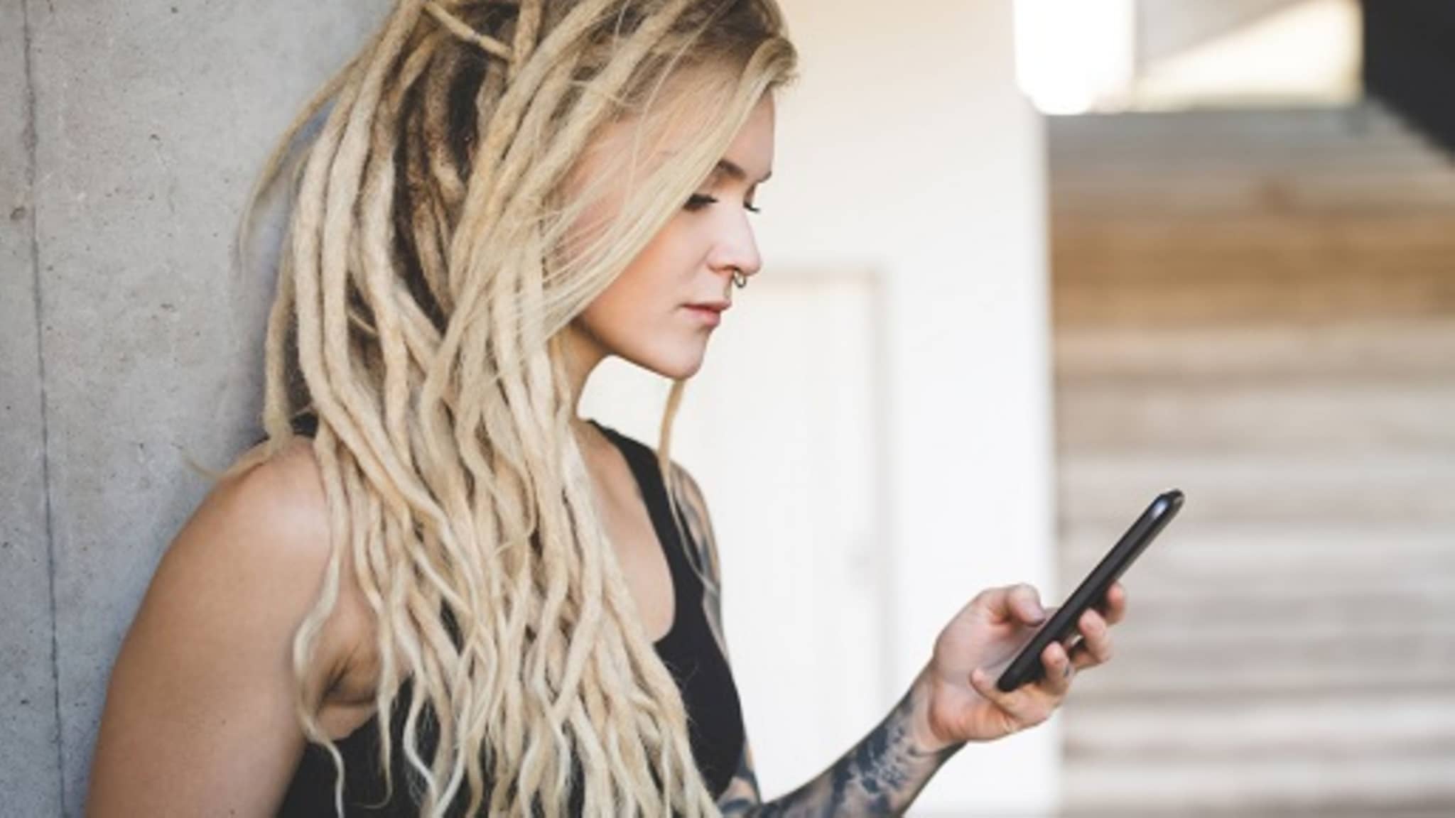 Junge Frau mit Dreadlocks checkt ihr Handy auf dem Campus.
