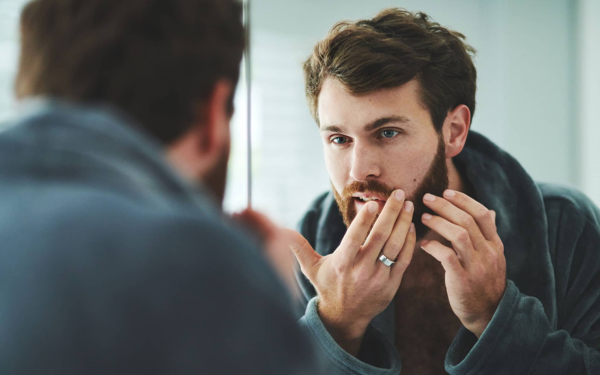 Mann prüft seine Haut kritisch im Spiegel.