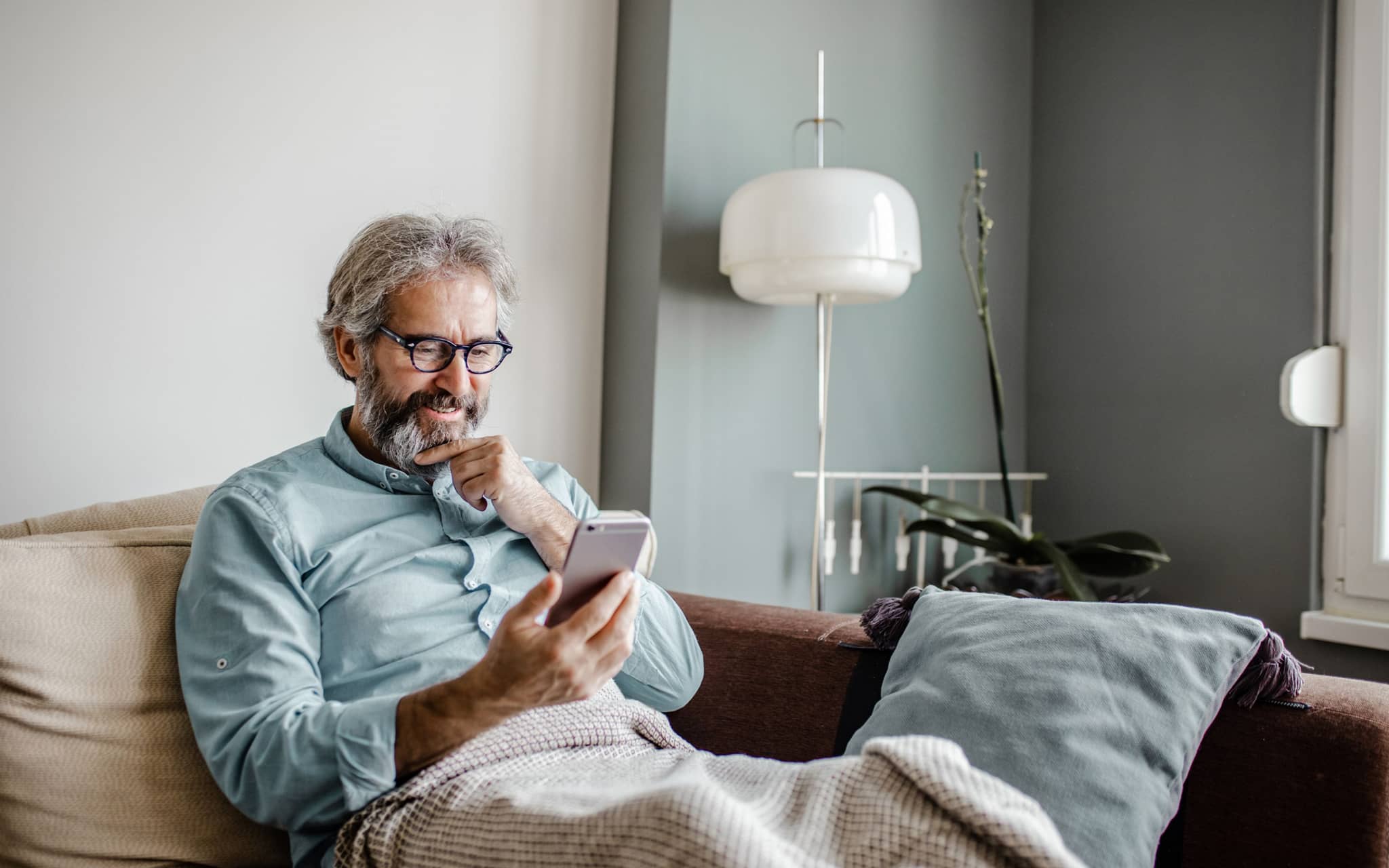 Zweitmeinung Gallenblase: Ein älterer Mann sitzt auf einem Sofa und liest auf seinem Smartphone