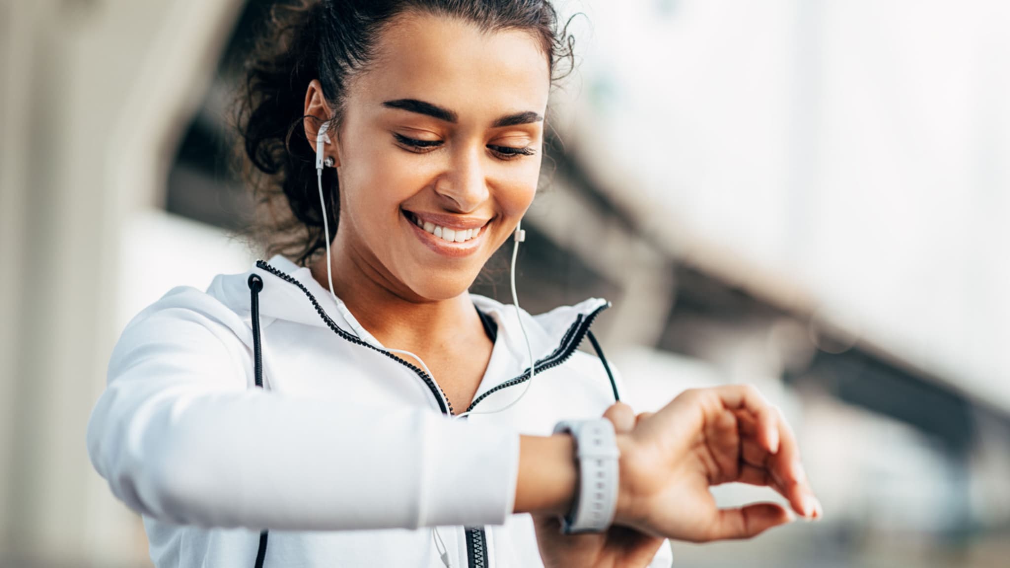 Eine sportlich bekleidete Frau blickt lächelnd auf Ihren Fitnesstracker.