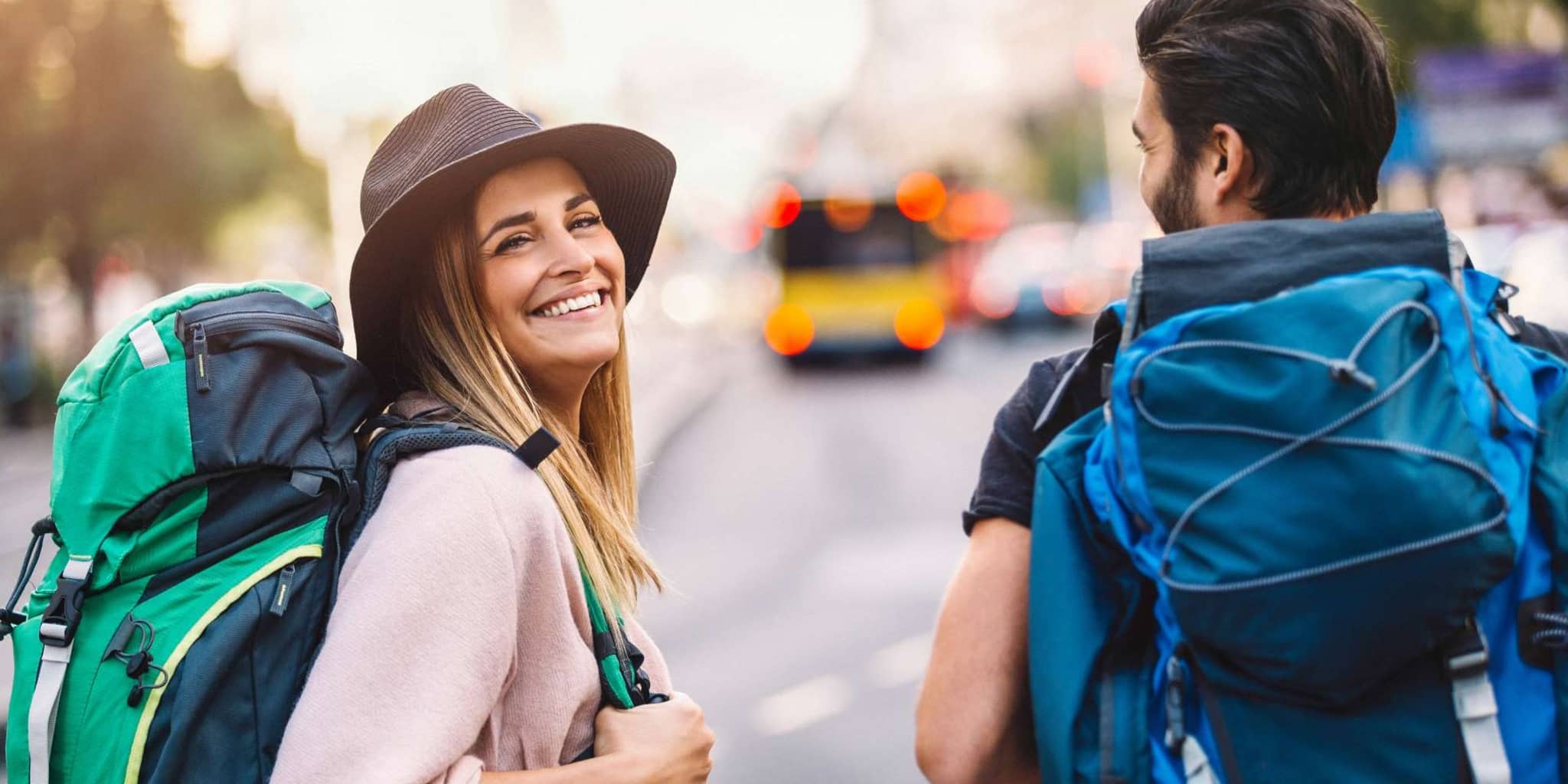 Fit & Travel: Junges Paar läuft im Urlaub mit Rucksäcken durch eine Stadt.
