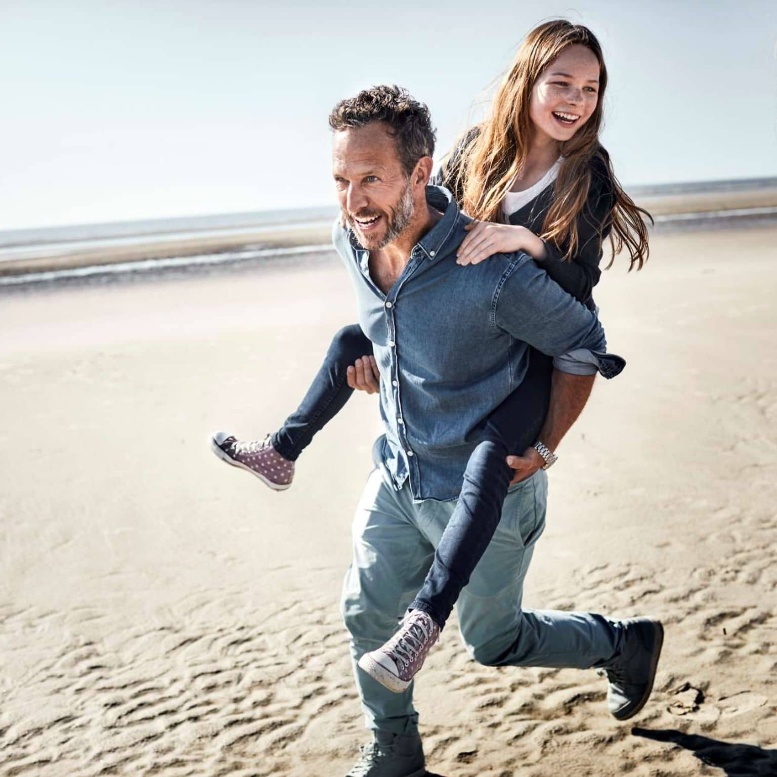 Bild: Vater trägt seine Tochter Huckepack am Strand