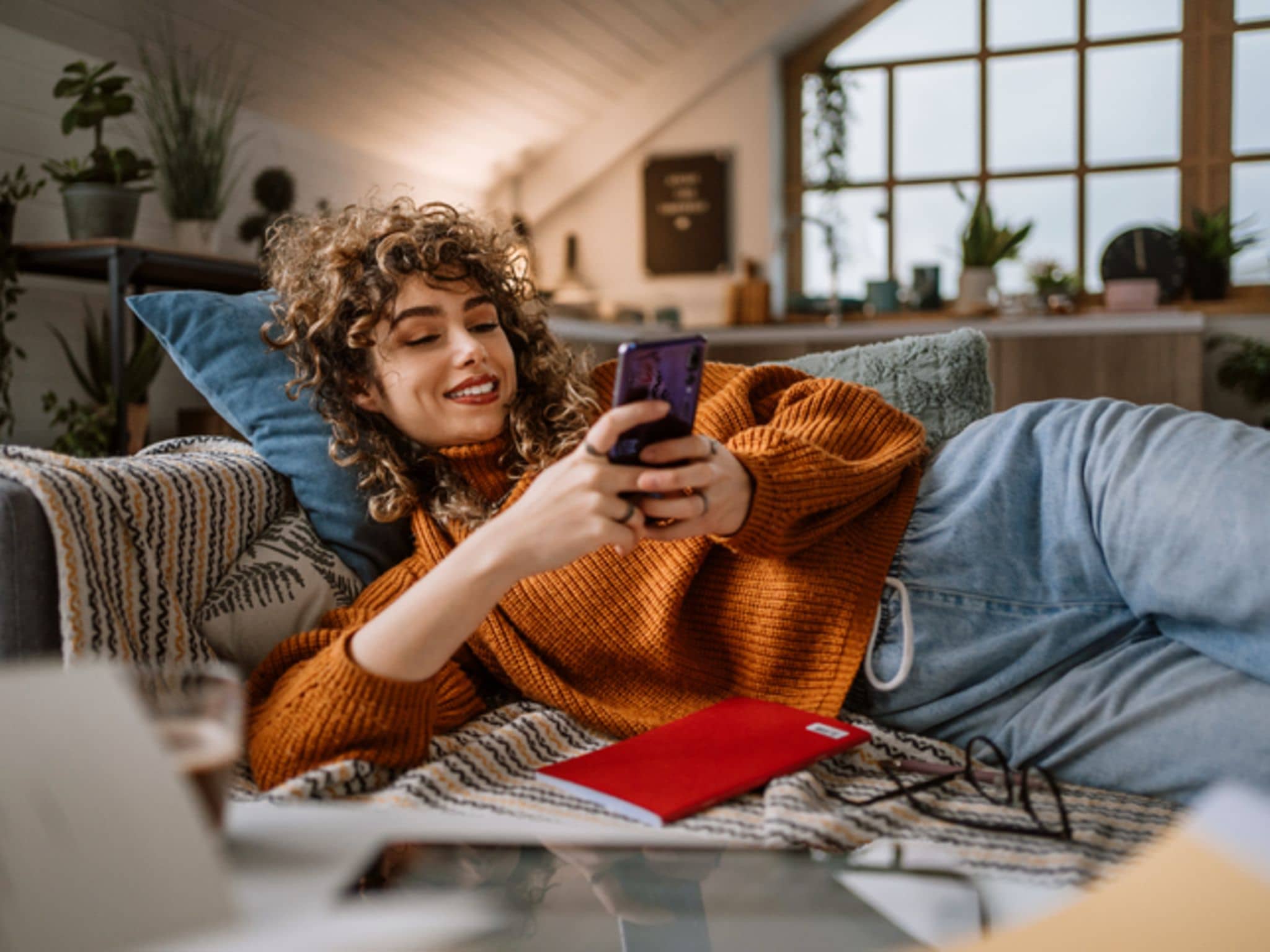 Symbolbild: Junge Frau mit Smartphone auf dem Sofa