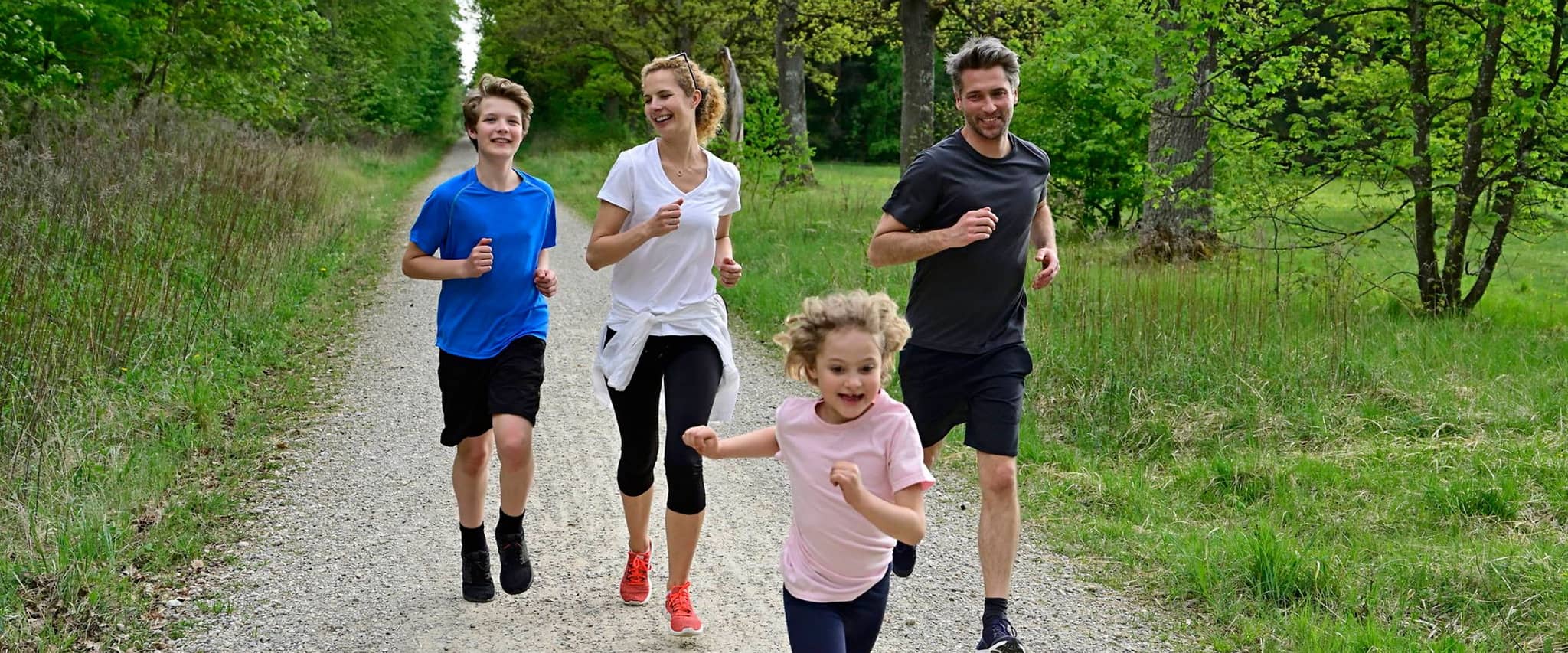 Bild: Vater, Mutter und zwei Kinder laufen auf einem Schotterweg in der Natur.