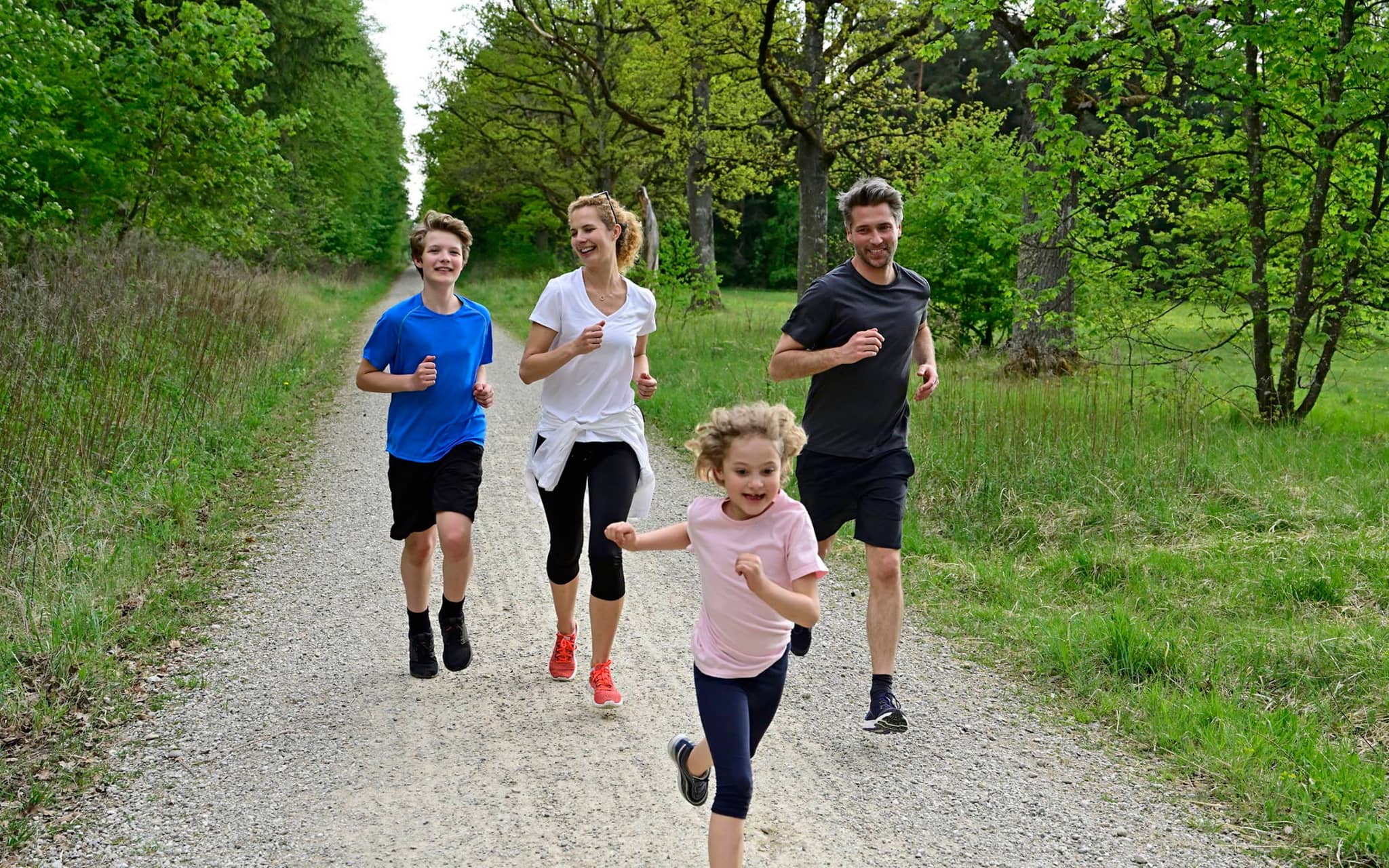 Bild: Vater, Mutter und zwei Kinder laufen auf einem Schotterweg in der Natur.