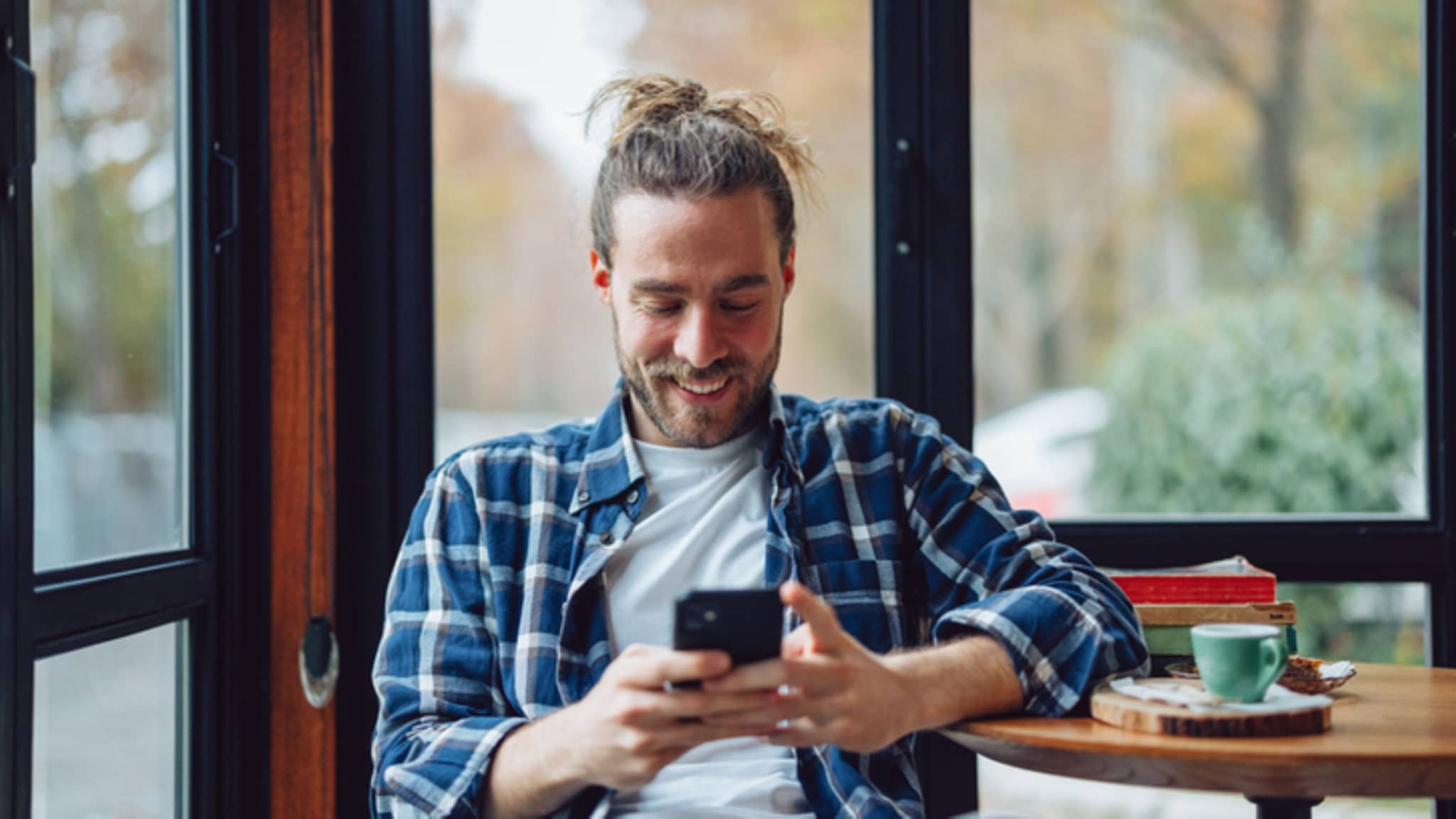 Mann sitzt auf Sofa und schaut lachend in sein Smartphone