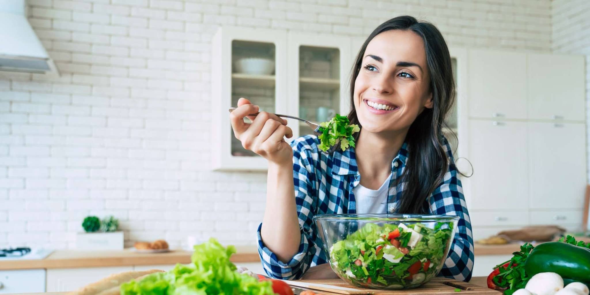 Fit & Cash: Junge Frau sitzt in ihrer Küche und isst einen Salat.