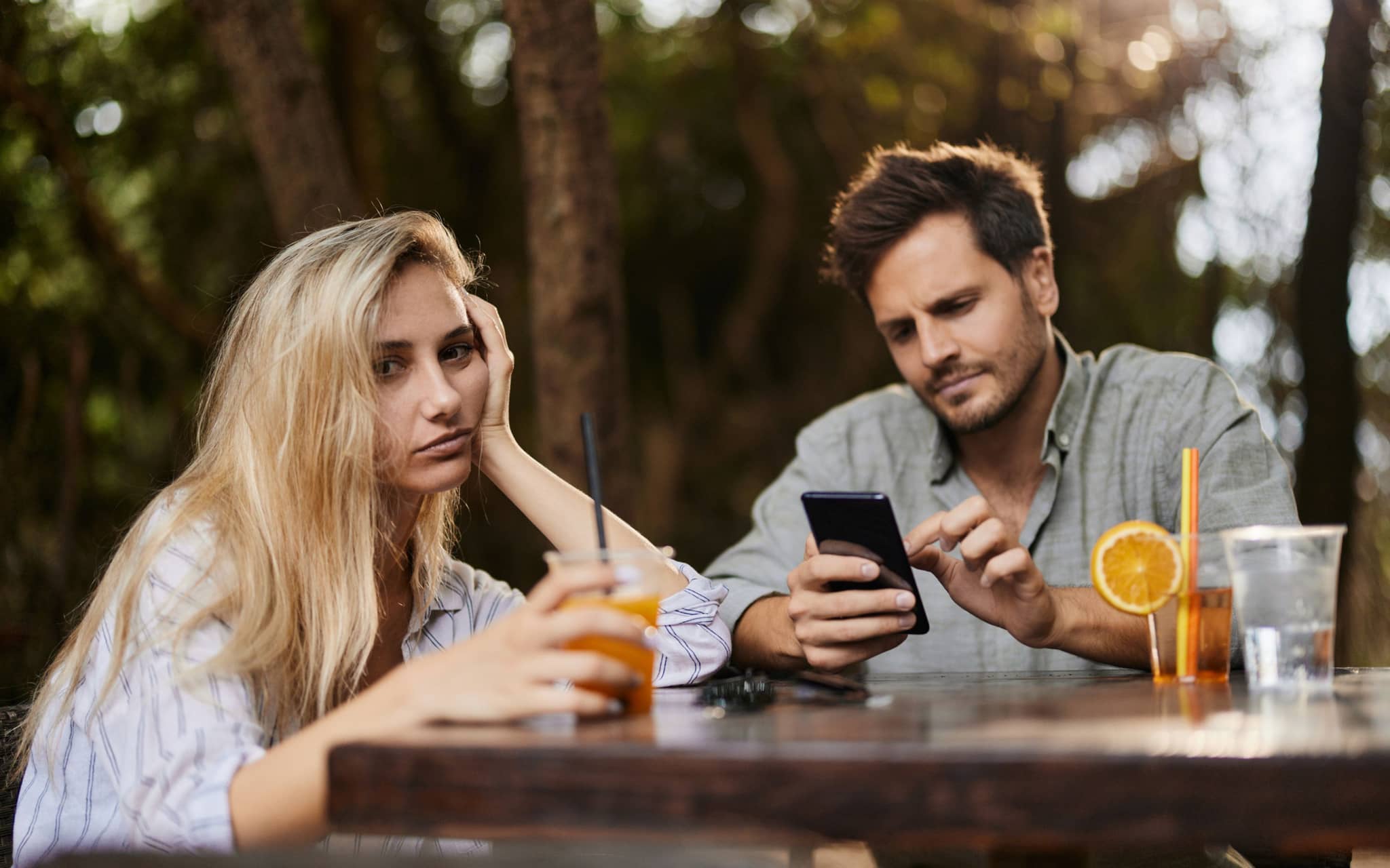 Eine Frau schaut genervt zur Seite, während ihr Partner Phubbing betreibt und am Smartphone hängt