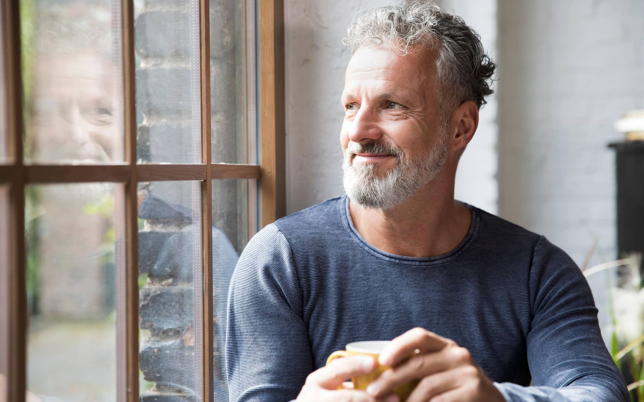 Wechseljahre beim Mann: Ein Mann mit grauen Schläfen guckt aus dem Fenster