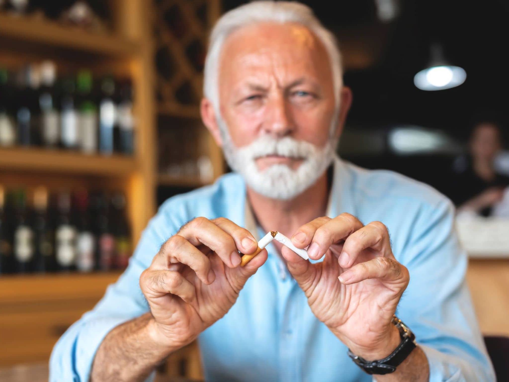 Älterer Mann sitzt in einem Restaurant und zerbricht eine Zigarette.