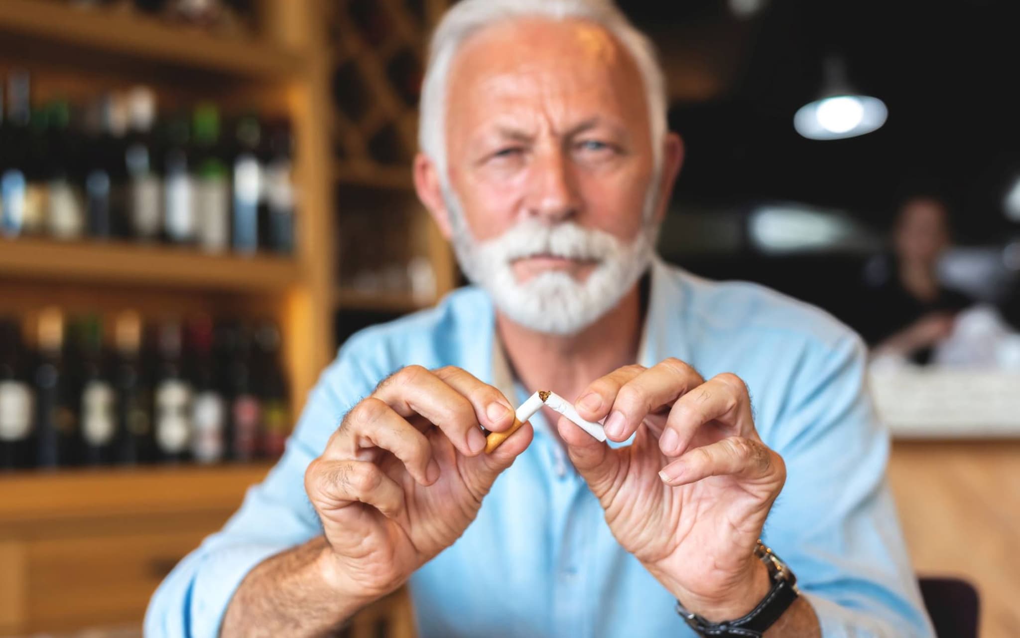 Älterer Mann sitzt in einem Restaurant und zerbricht eine Zigarette.
