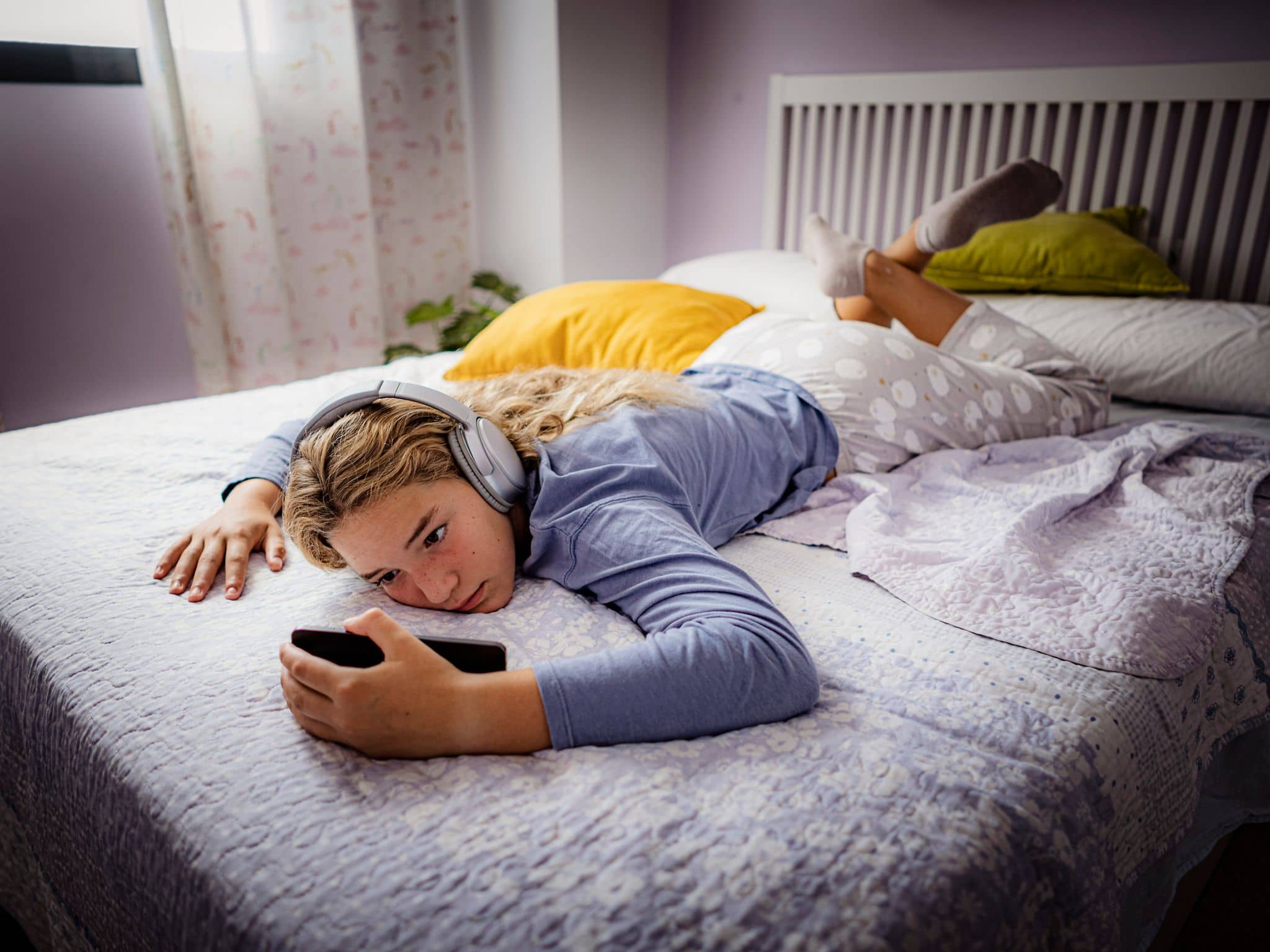 Mediensucht-Hotline: Mädchen liegt mit Kopfhörern im Bett und starrt aufs Smartphone.