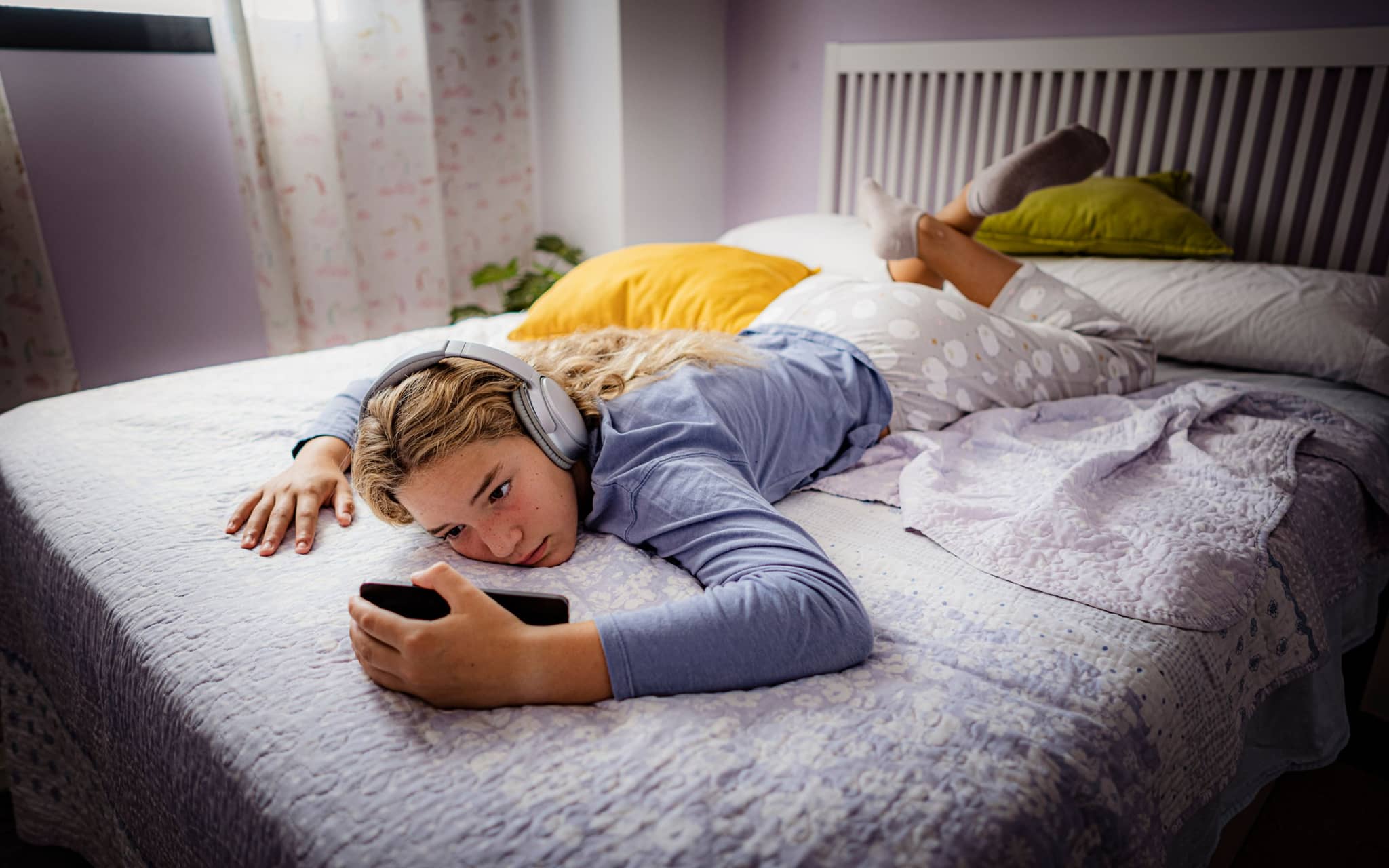 Mediensucht-Hotline: Mädchen liegt mit Kopfhörern im Bett und starrt aufs Smartphone.