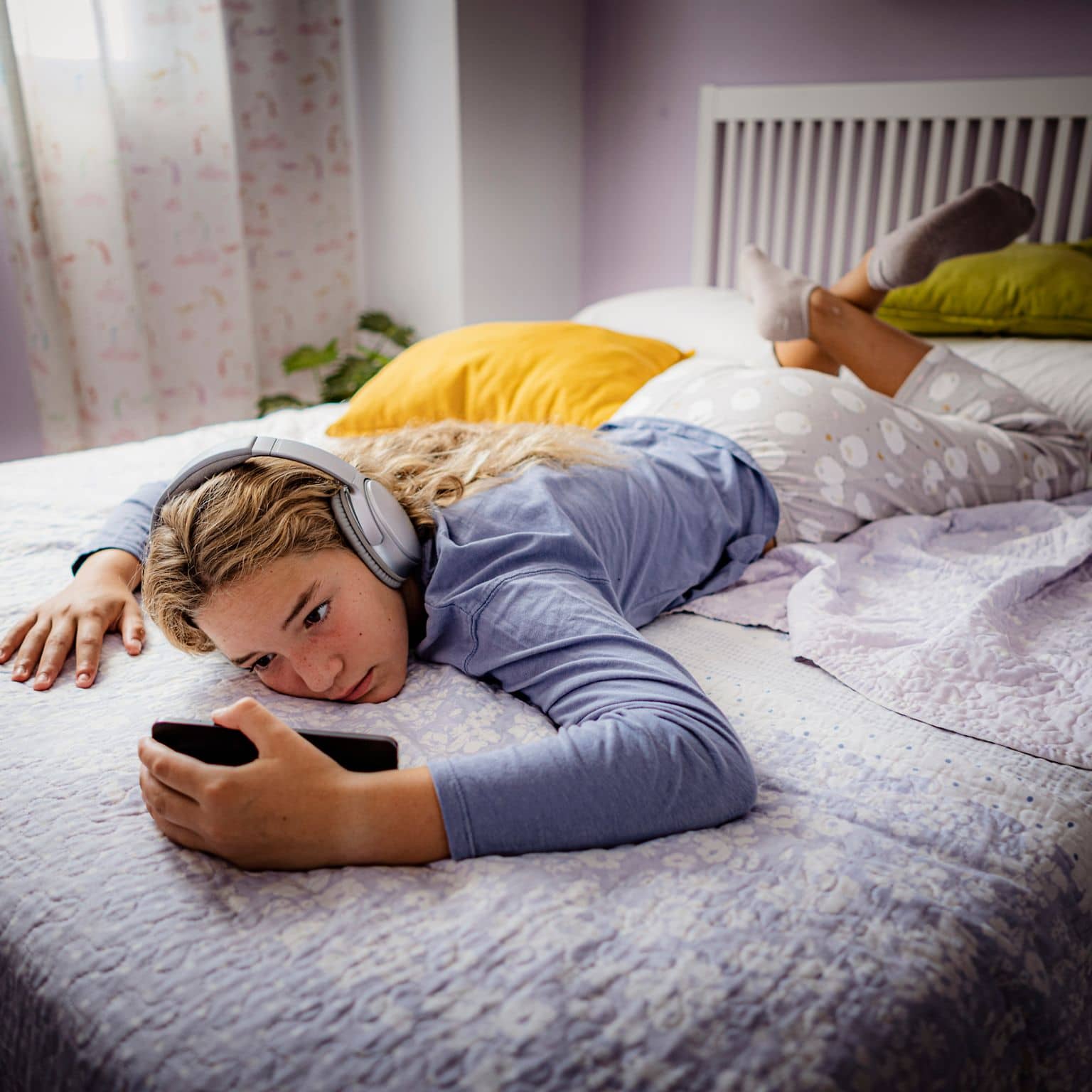 Mediensucht-Hotline: Mädchen liegt mit Kopfhörern im Bett und starrt aufs Smartphone.