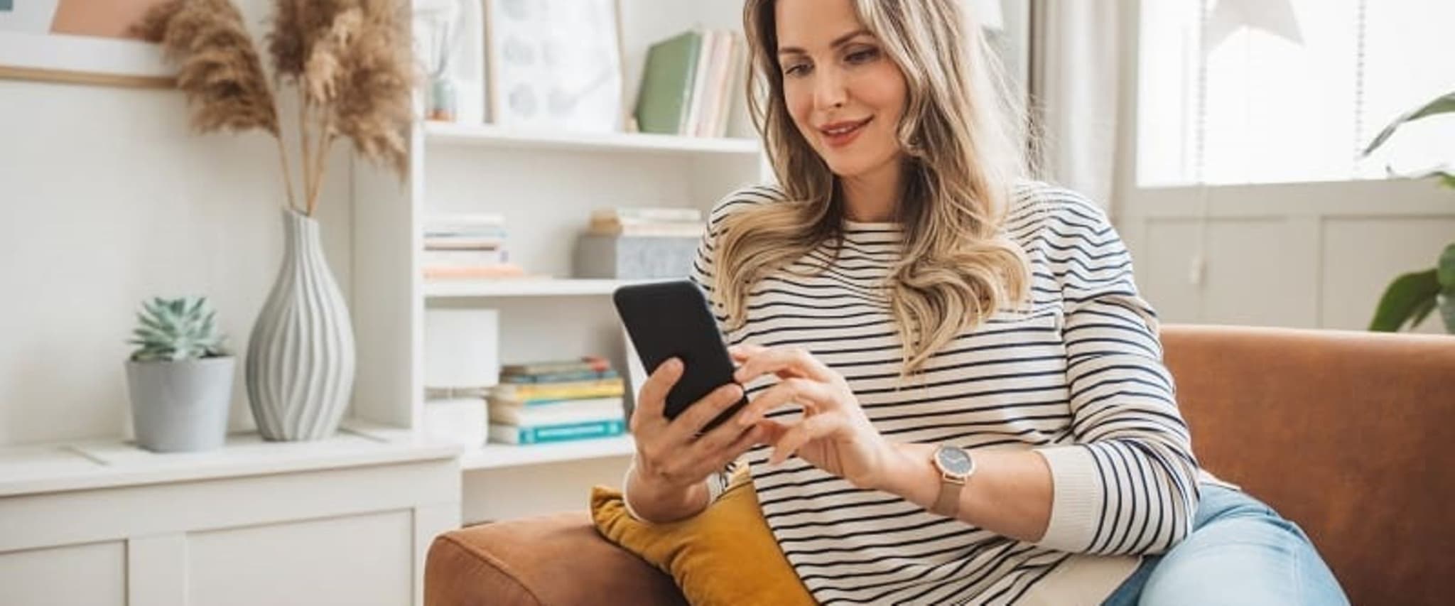 Frau erledigt ihr Anliegen mit dem Handy auf dem Sofa mithilfe der DAK App.