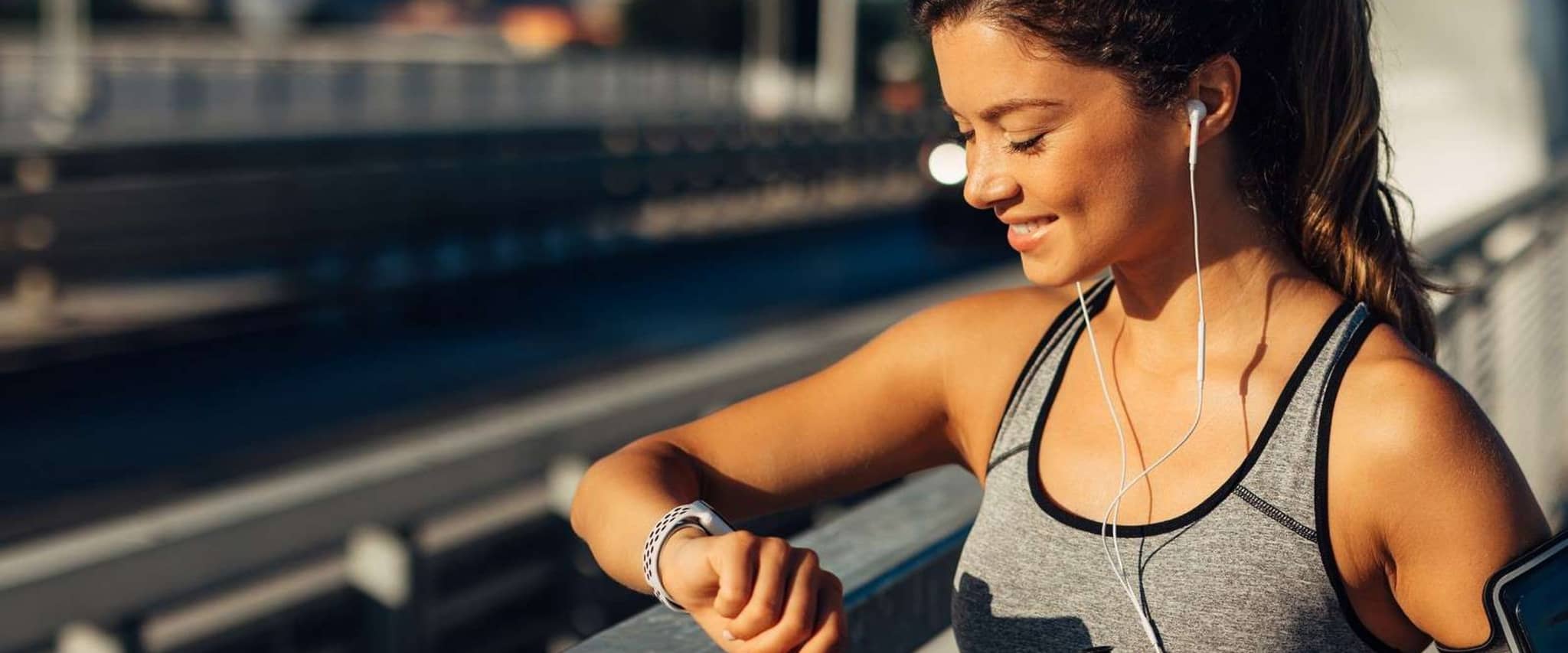 DAK AktivBonus: Junge Frau schaut während einer Pause beim Joggen auf ihre Fitnessuhr.