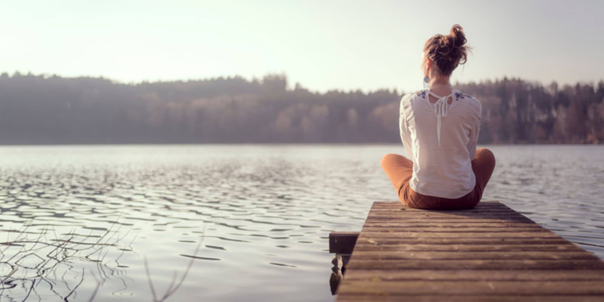 Frau sitzt an einem See auf Steg