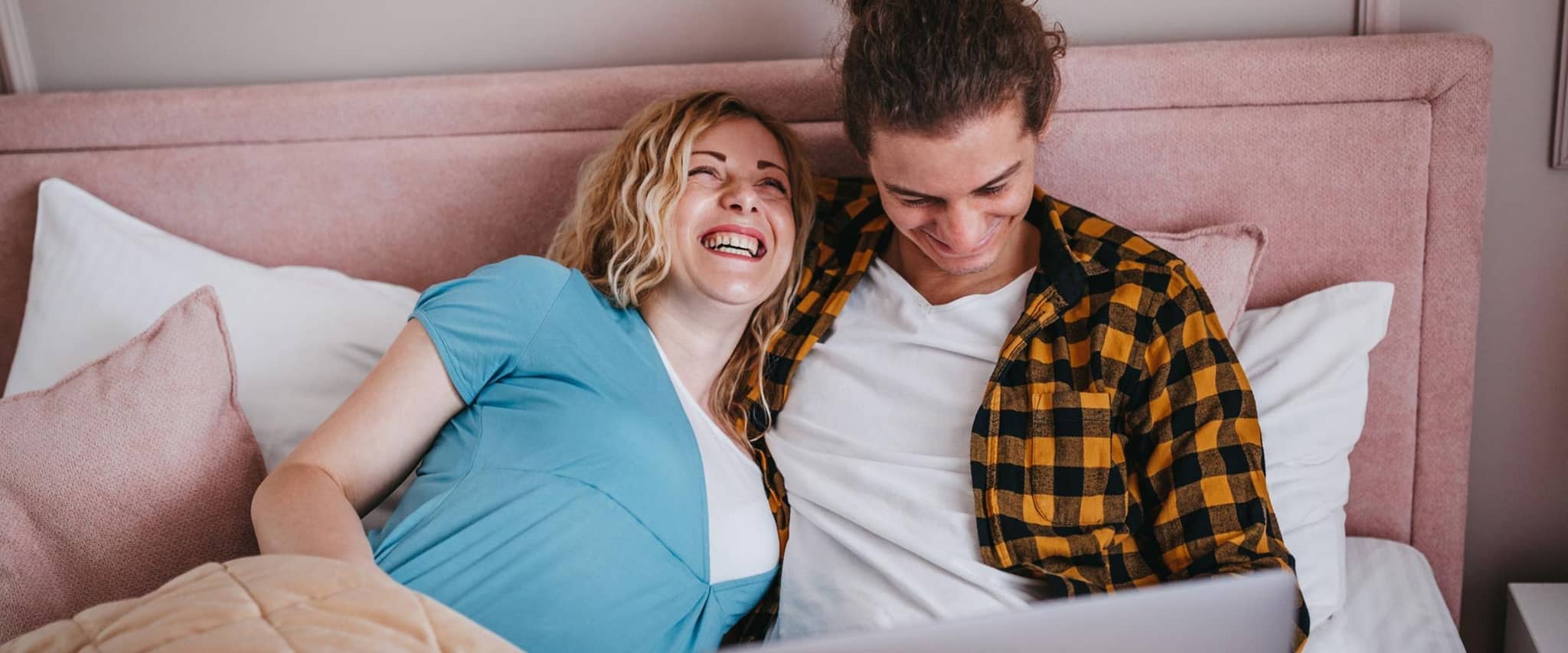 Junges schwangeres Paar liegt zuhause im Bett und schaut auf ein Notebook.