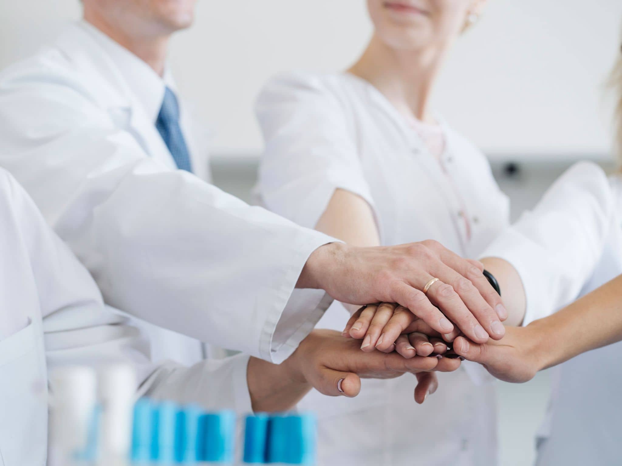 Mehrere Medizinerinnen und Mediziner stapeln Ihre Hände übereinander als Symbol für Teamwork.