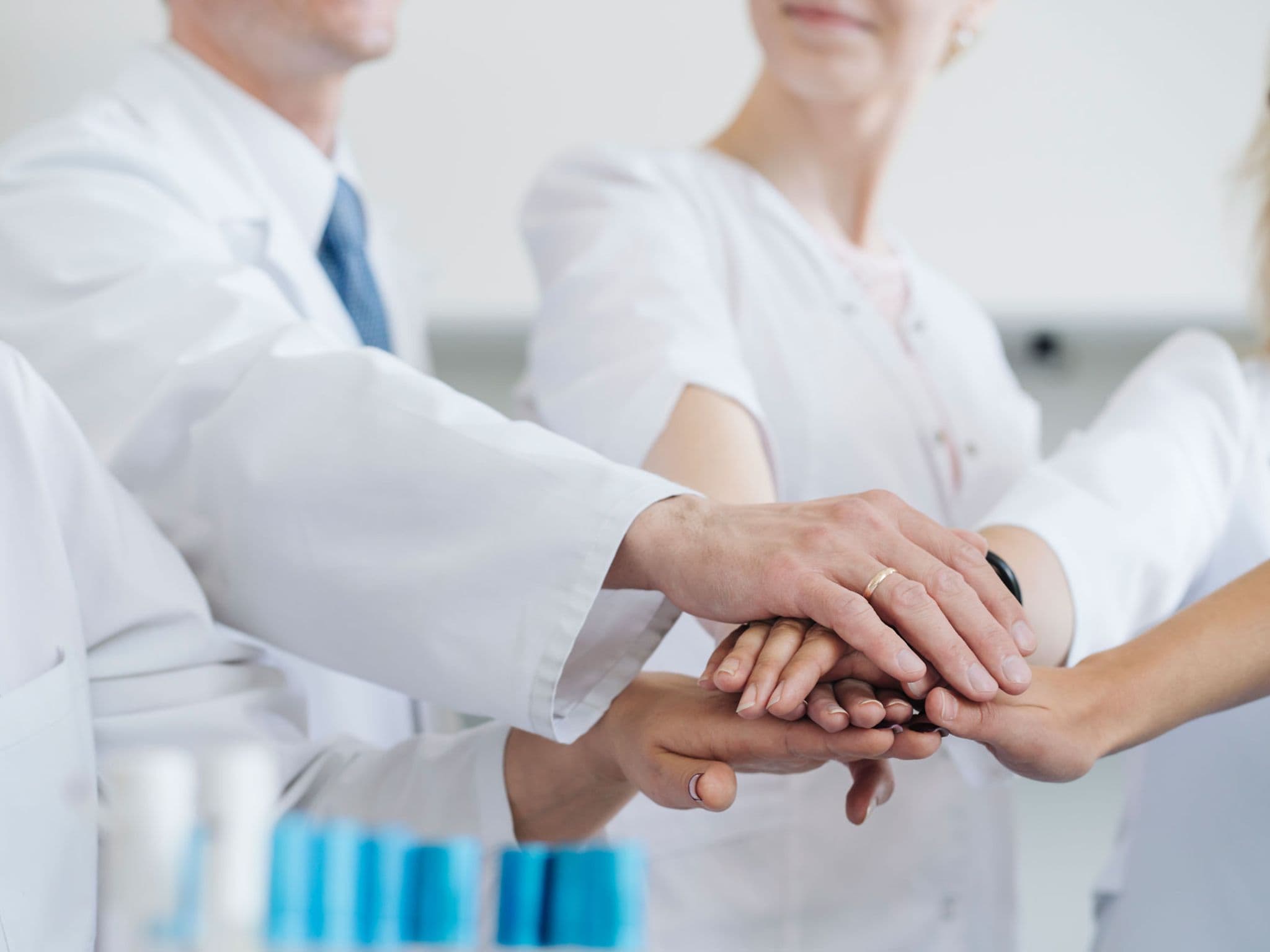 Mehrere Medizinerinnen und Mediziner stapeln Ihre Hände übereinander als Symbol für Teamwork.