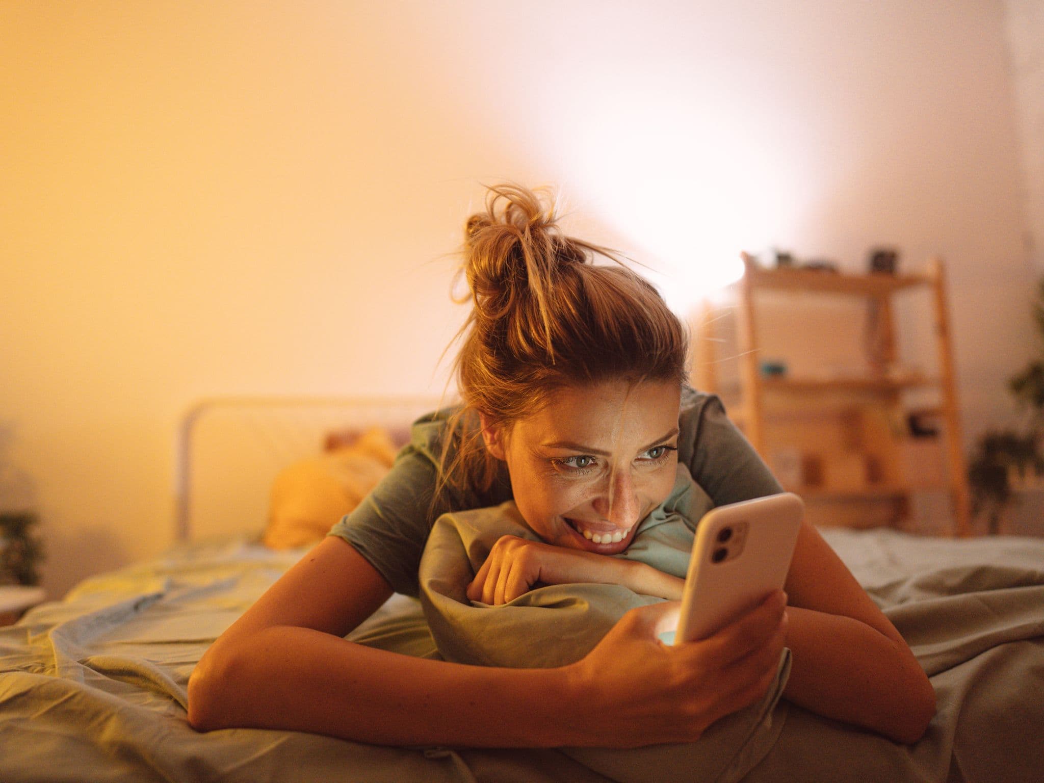 Online-Dating: Eine junge Frau liegt auf ihrem Bett und guckt auf ihrem Handy nach Matches