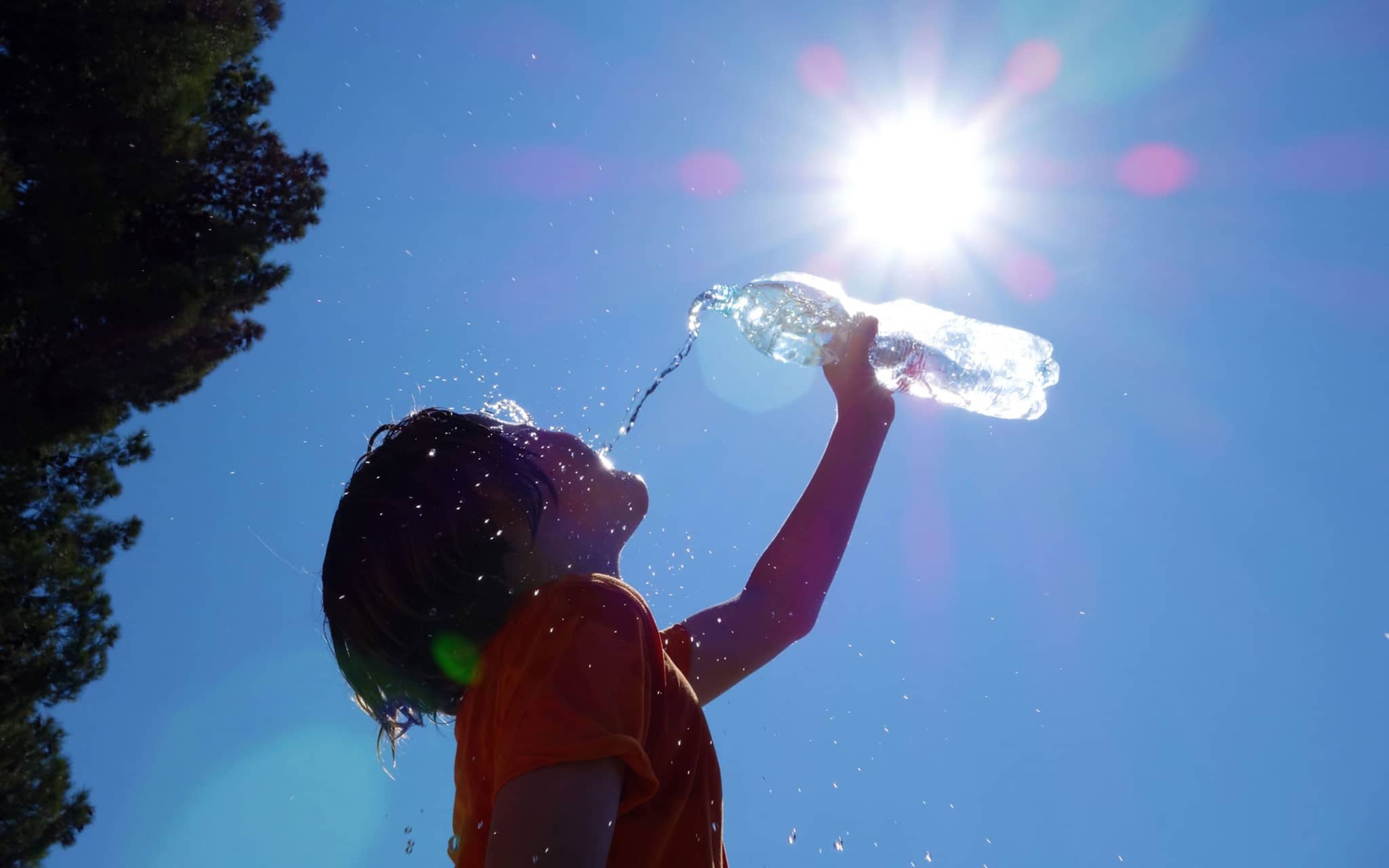 Hitze: Kind steht draußen in der Sonne und trinkt aus einer Wasserflasche.