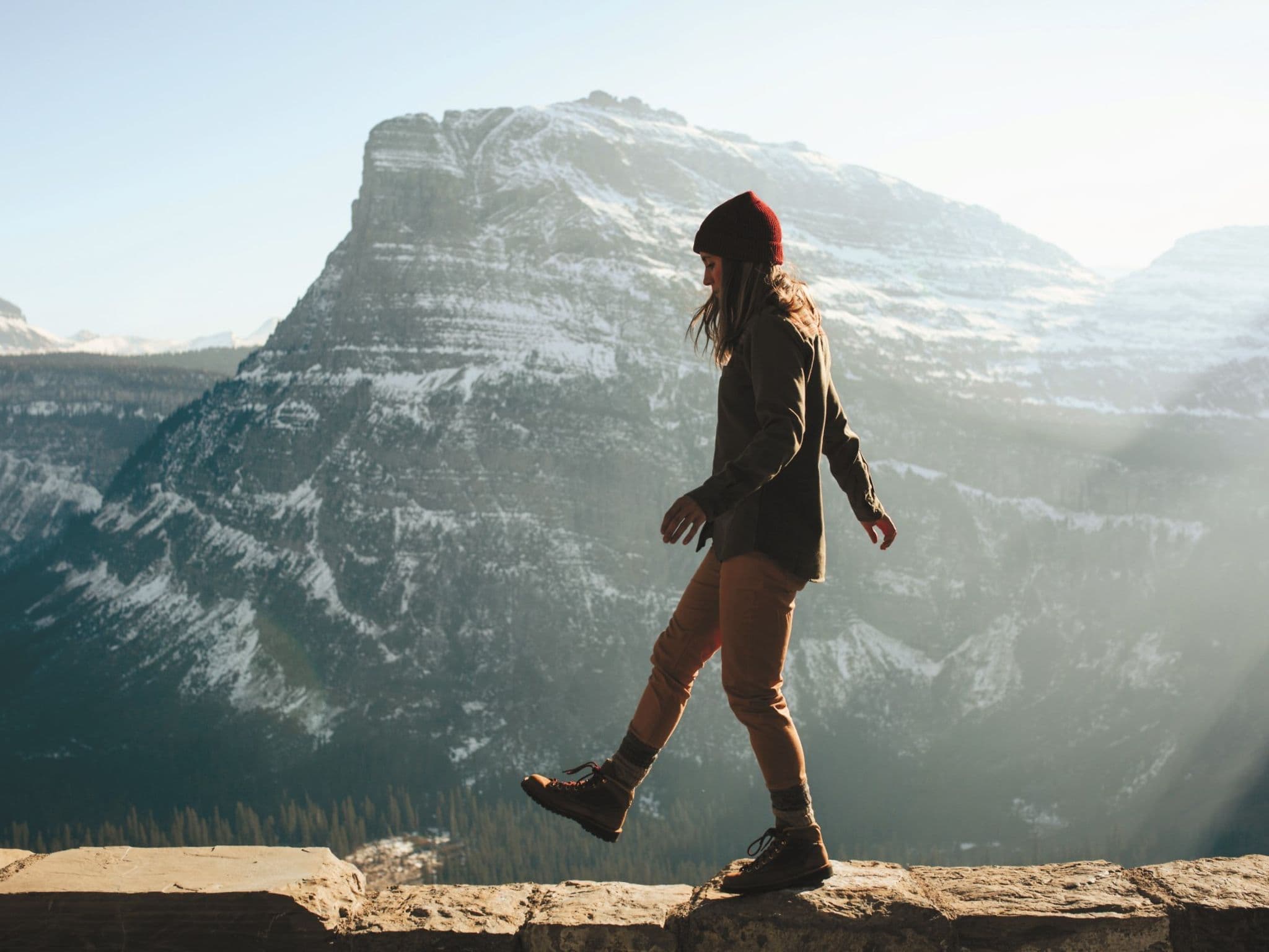 Woman walking on ledge against a beautiful blue mountain range.