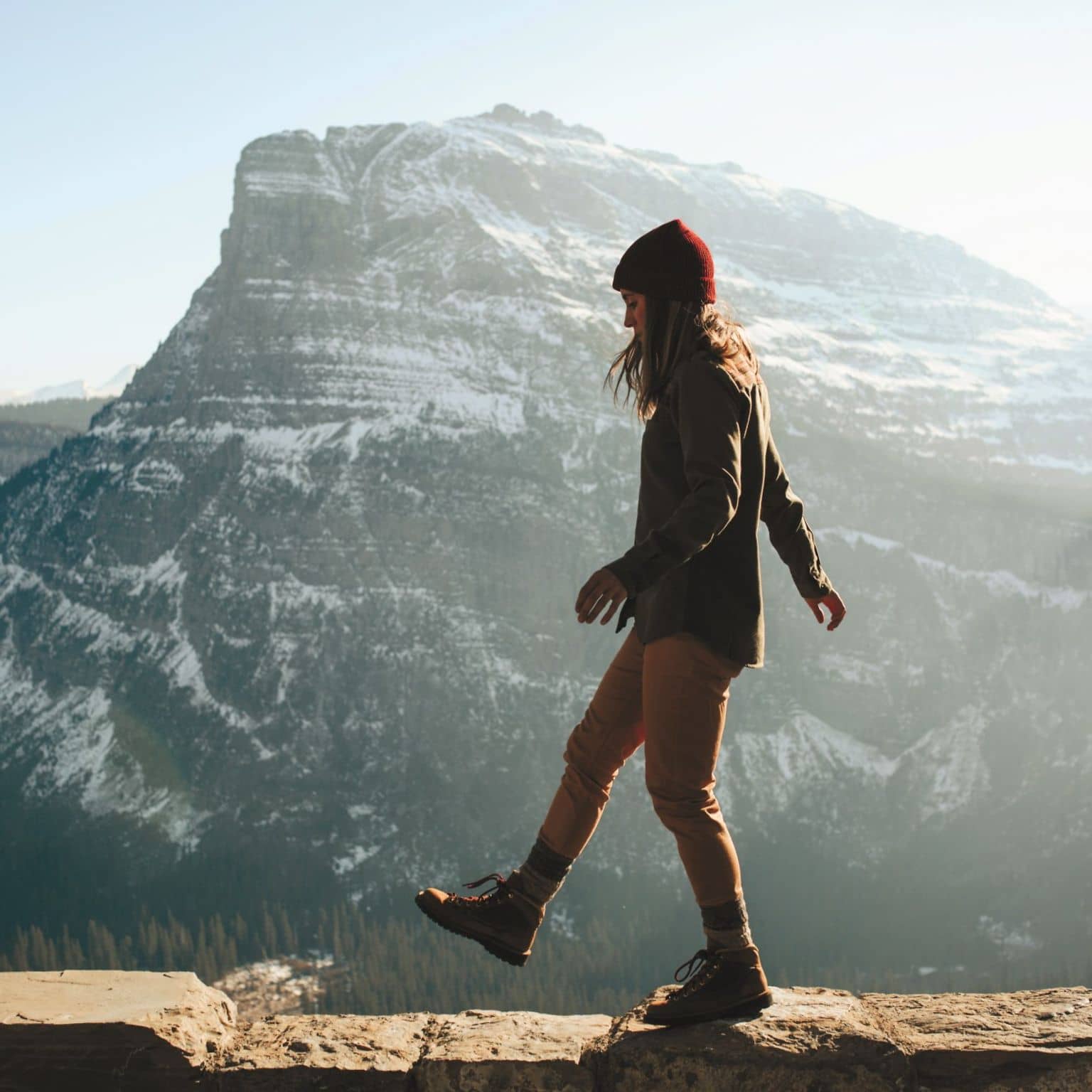 Woman walking on ledge against a beautiful blue mountain range.