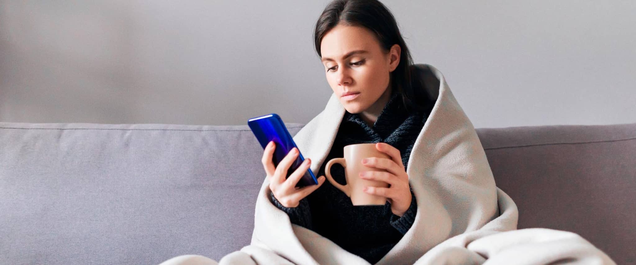 Frau sitzt auf dem Sofa zuhause und nutzt die Videosprechstunde.