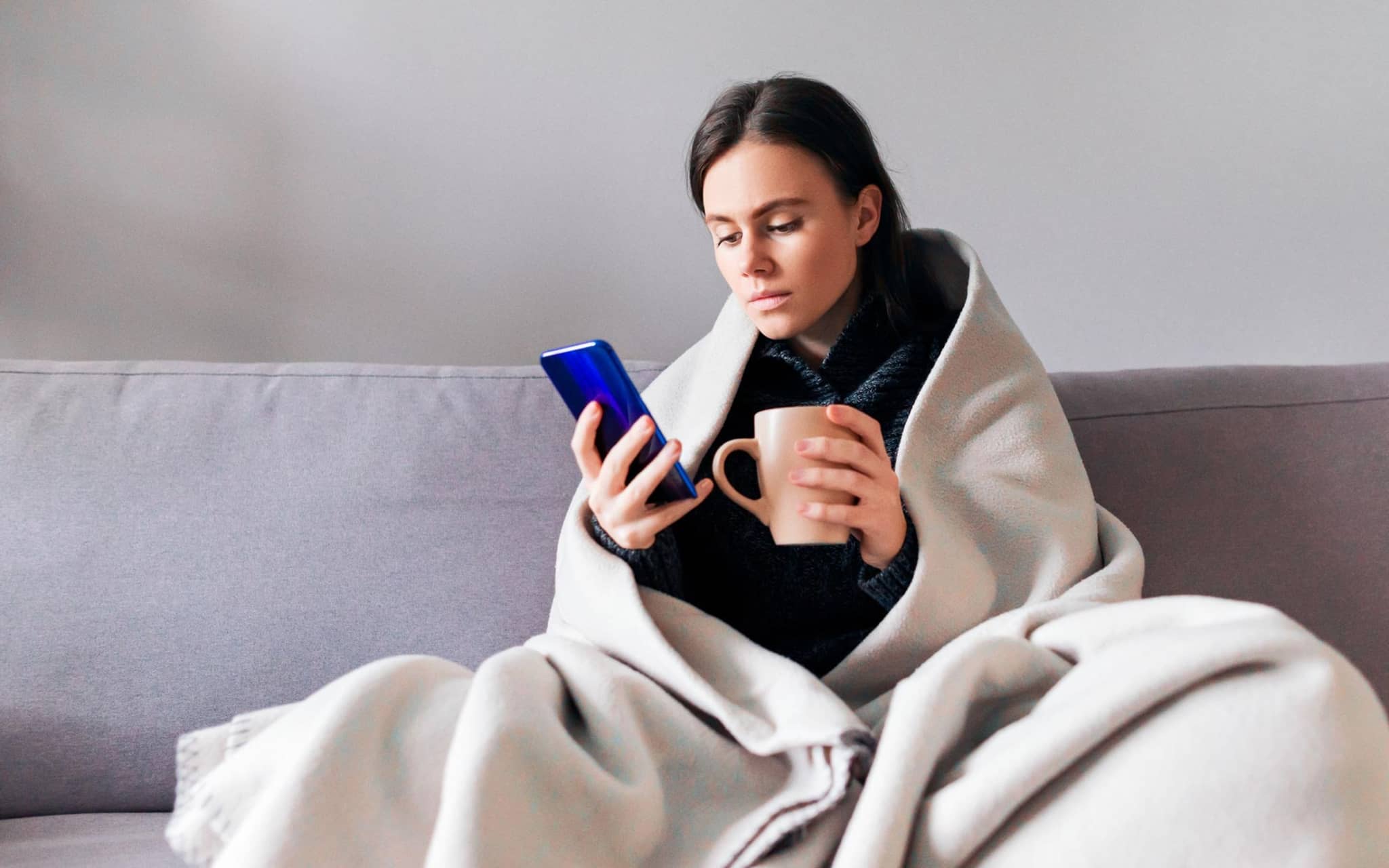 Frau sitzt auf dem Sofa zuhause und nutzt die Videosprechstunde.