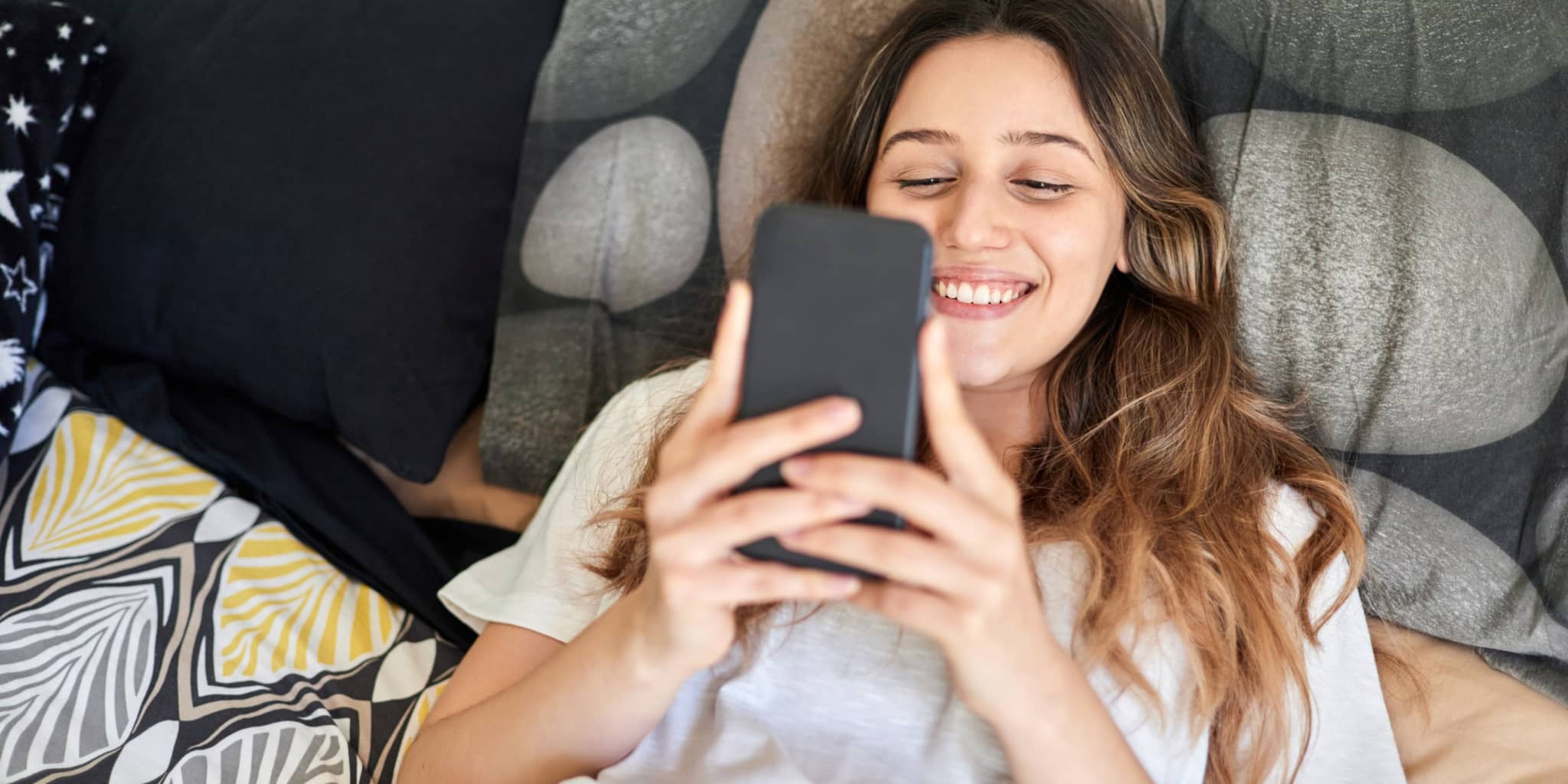 Junge Frau liegt auf dem Sofa und schaut auf ihr Handy.