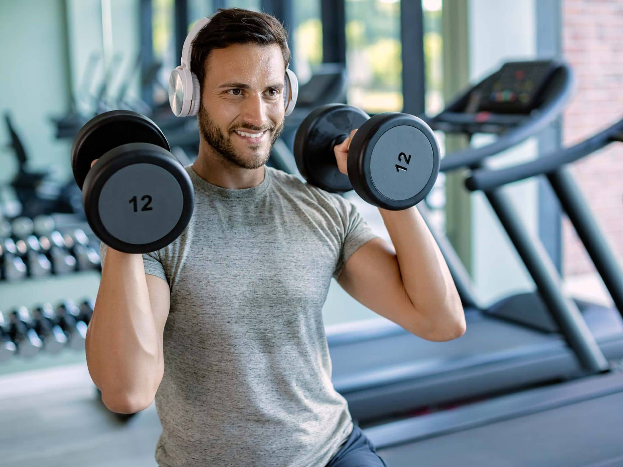 Junger Mann stemmt zwei Hanteln in einem Fitnessstudio.