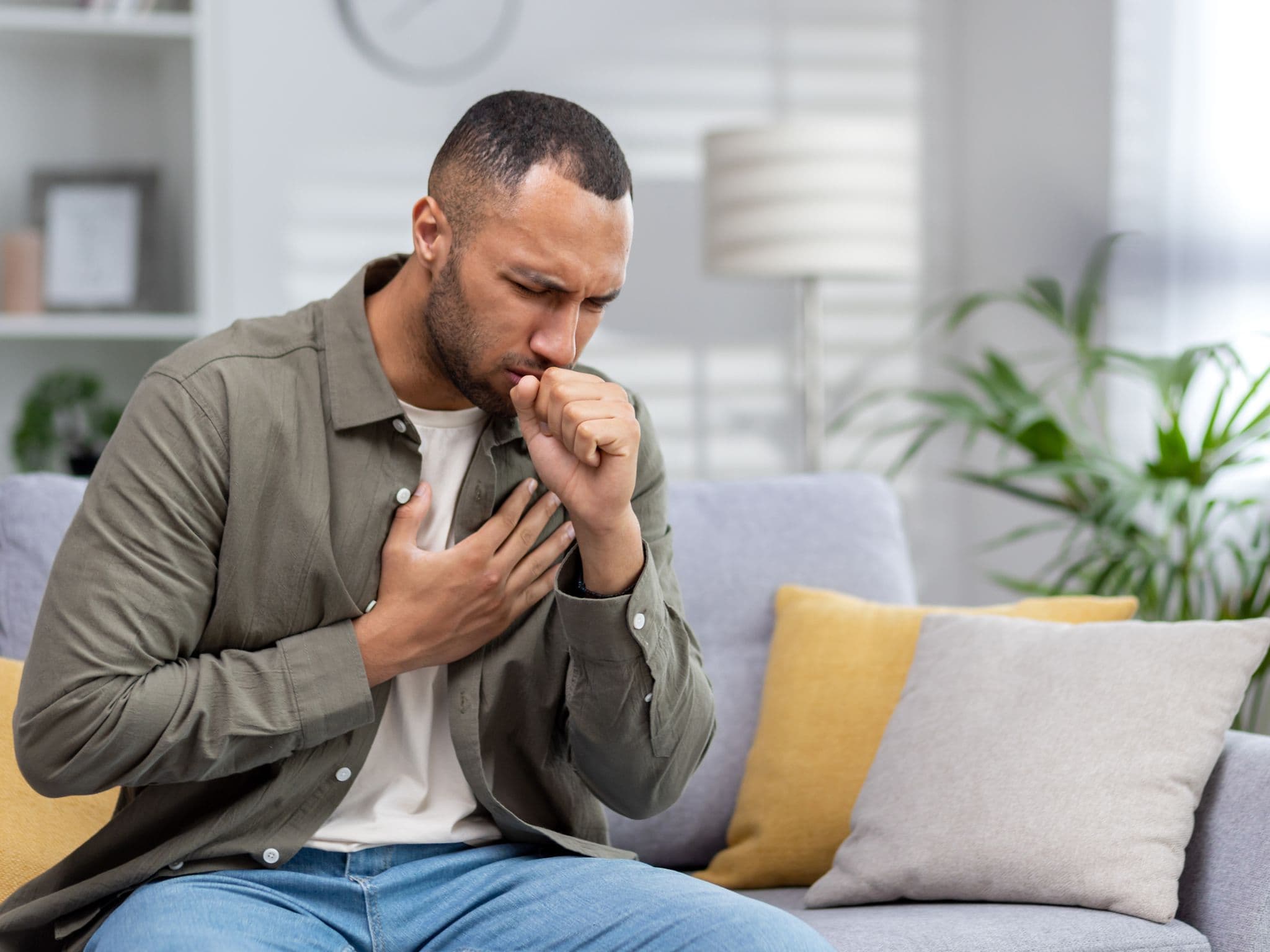 Bild: Mann hustet und fasst sich an die Brust. Könnte eine Bronchitis sein.