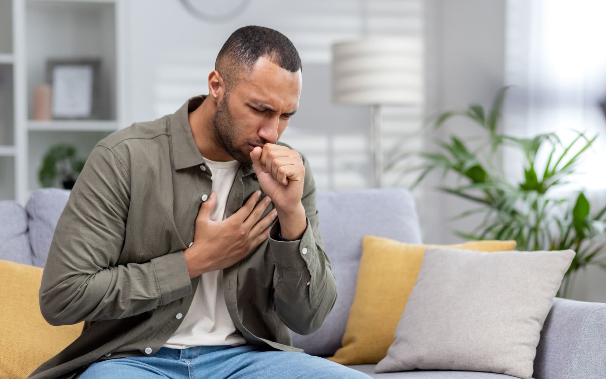 Bild: Mann hustet und fasst sich an die Brust. Könnte eine Bronchitis sein.