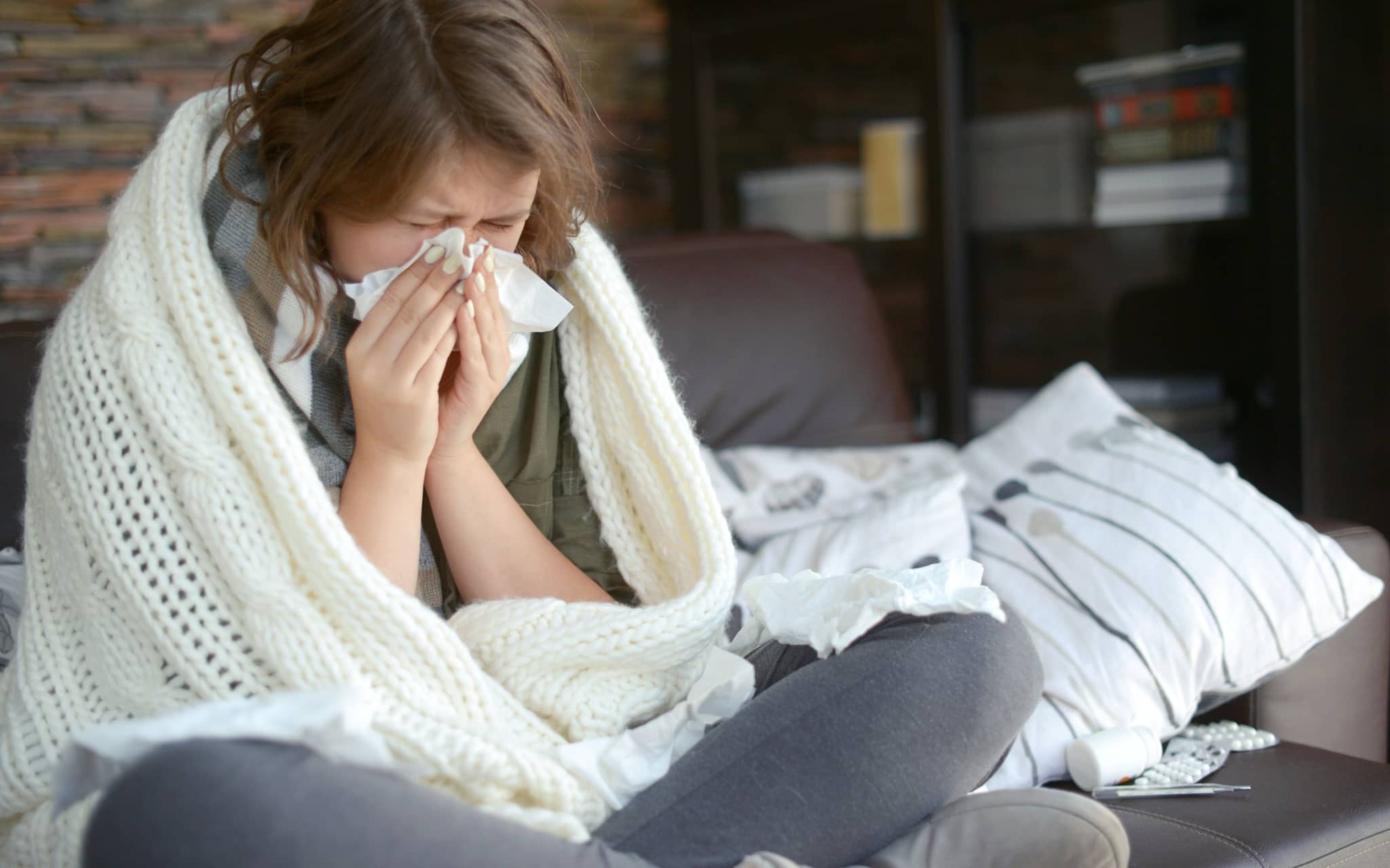 Ständig erkältet: Eine junge Frau sitzt auf einem Sofa und schnupft in ihr Taschentuch