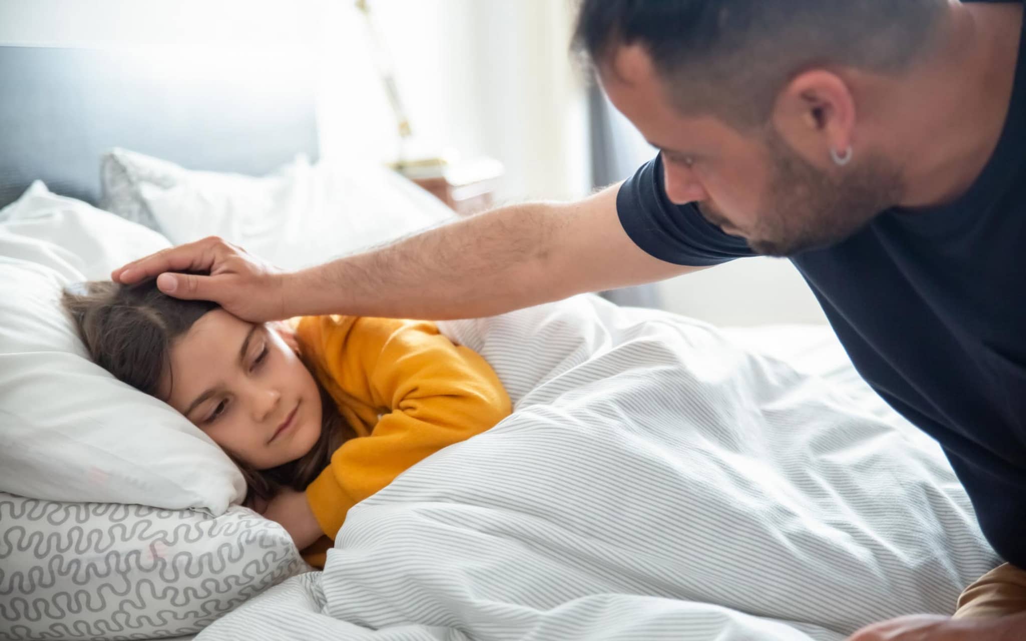 Scharlach: Ein Vater fasst seiner kranken, im Bett liegenden Tochter an die Stirn.