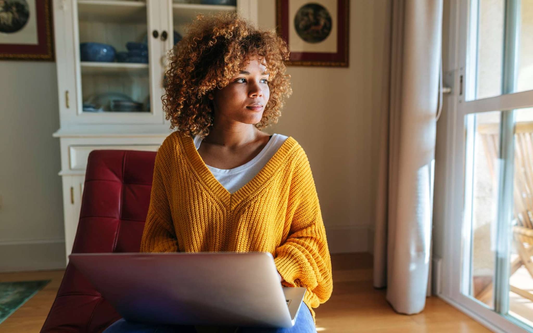 CIRS: Junge Frau sitzt zuhause vor ihrem Notebook und schaut aus dem Fenster.