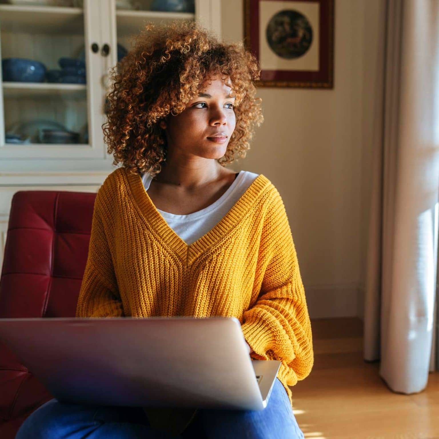 CIRS: Junge Frau sitzt zuhause vor ihrem Notebook und schaut aus dem Fenster.