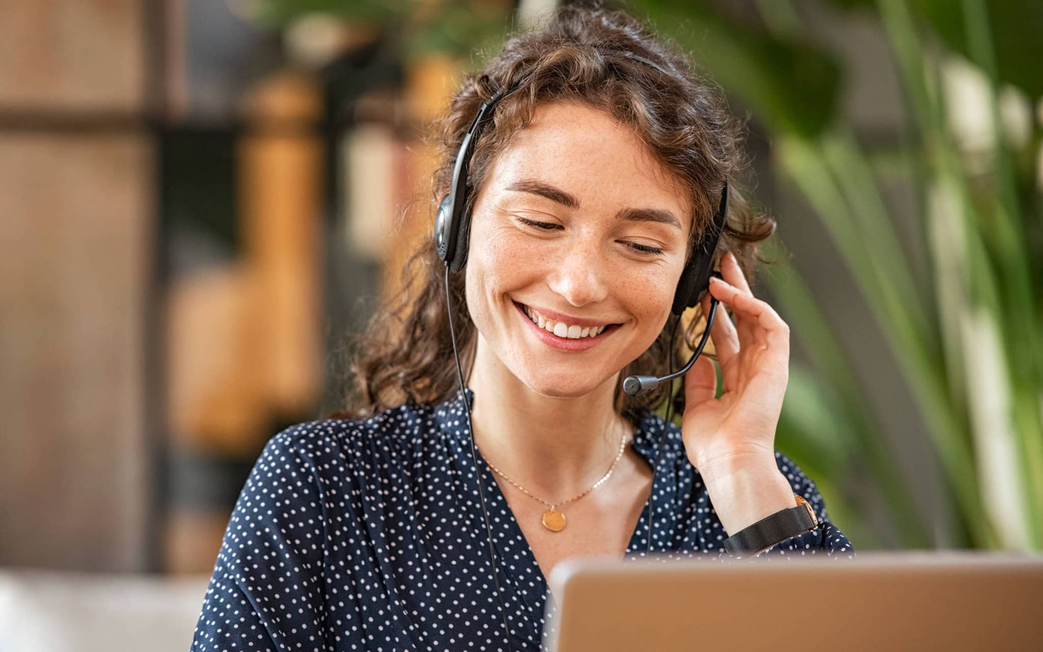 Lächelnde Frau mit Headset sitzt am Tisch und führt ein Gespräch, vermutlich im Kundenservice oder Callcenter.