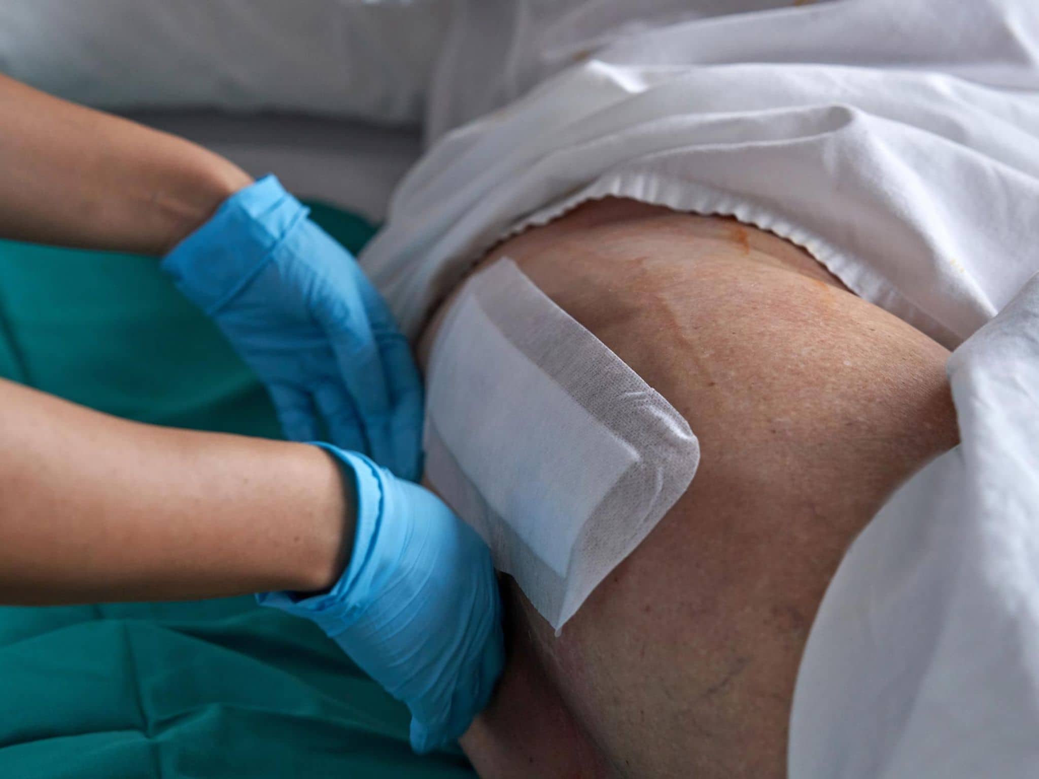 Versorgungsreport: Die Hände einer Krankenpflegerin legen am Bein eines Patienten ein Wundpflaster an.