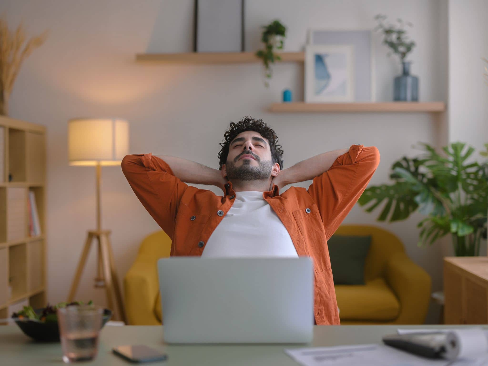 Junger Mann sitzt am Schreibtisch und verschränkt während einer Pause die Arme hinter dem Kopf.