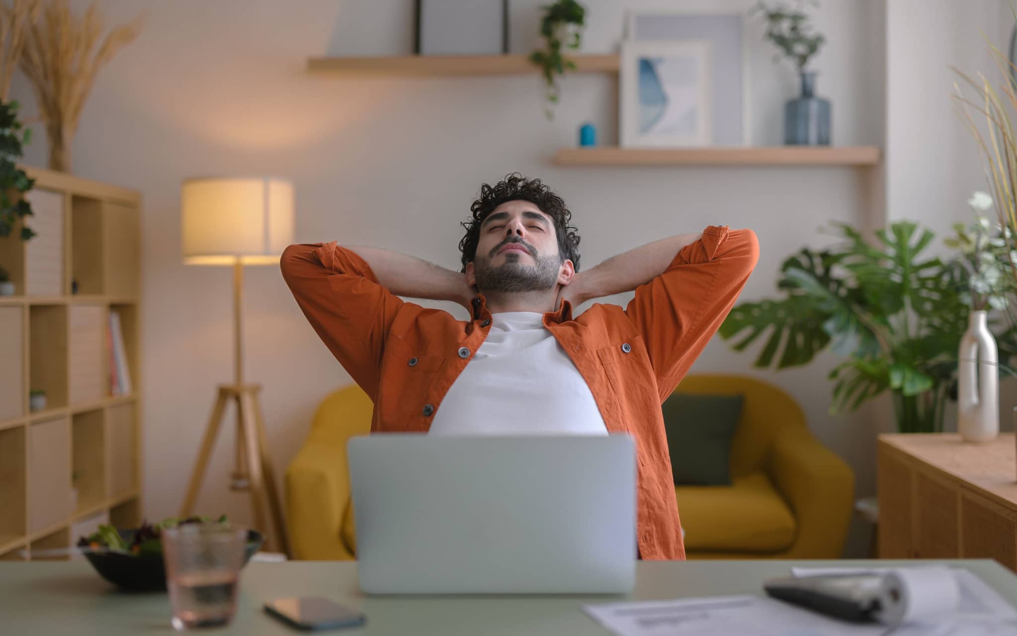 Junger Mann sitzt am Schreibtisch und verschränkt während einer Pause die Arme hinter dem Kopf.