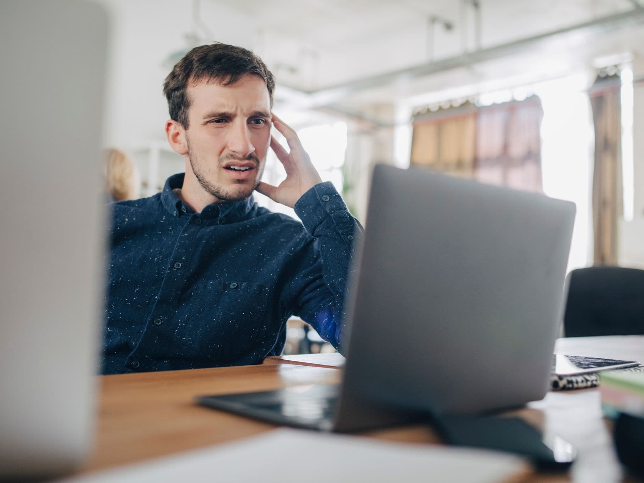 Mann sitzt vor dem Laptop und guckt irritiert.