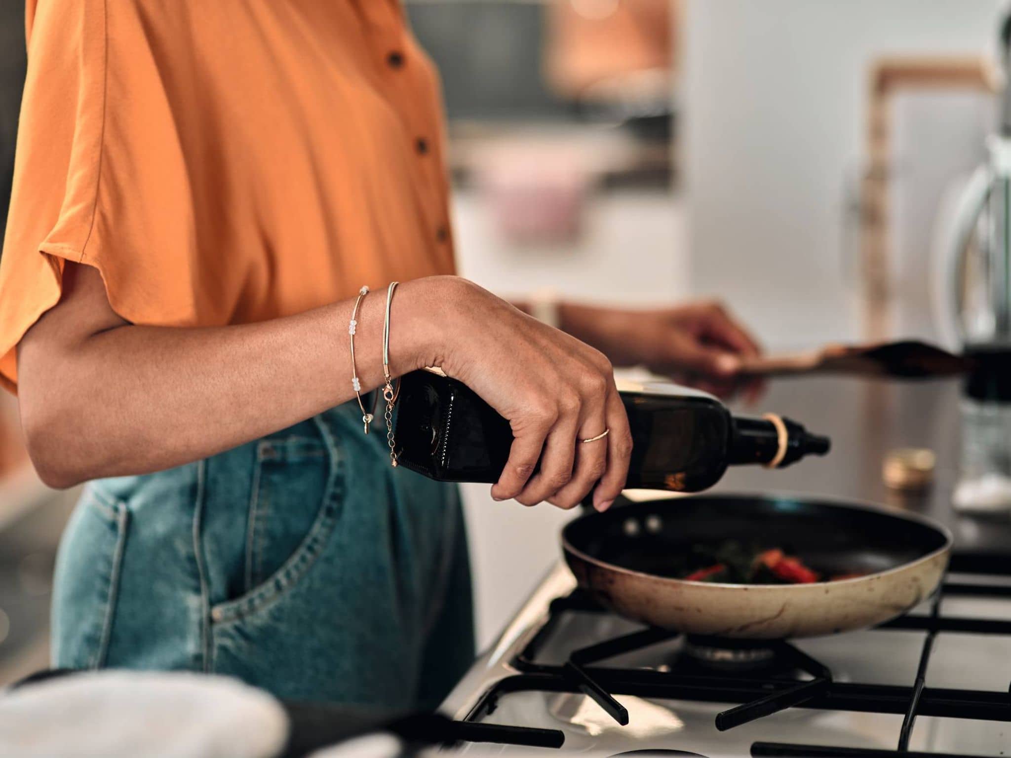 Bild: Nahaufnahme einer Frau, die gerade etwas Öl in eine Pfanne gibt.