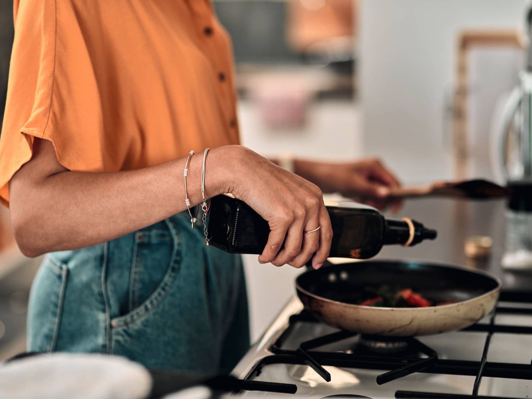 Bild: Nahaufnahme einer Frau, die gerade etwas Öl in eine Pfanne gibt.