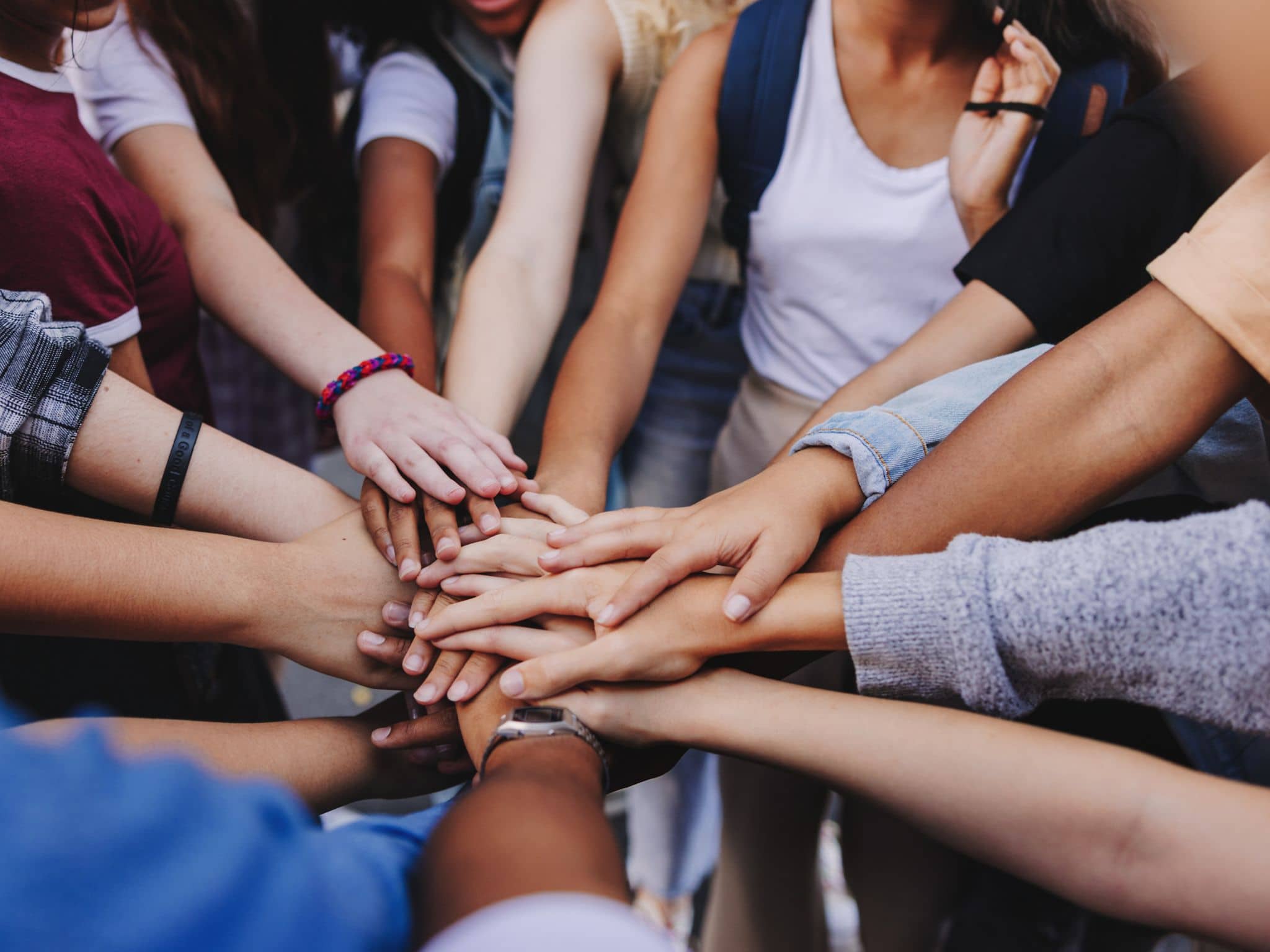 Bild: Menschen mit unterschiedlicher Hautfarbe legen die Hände übereinander, um gemeinsames Handeln zu signalisieren.