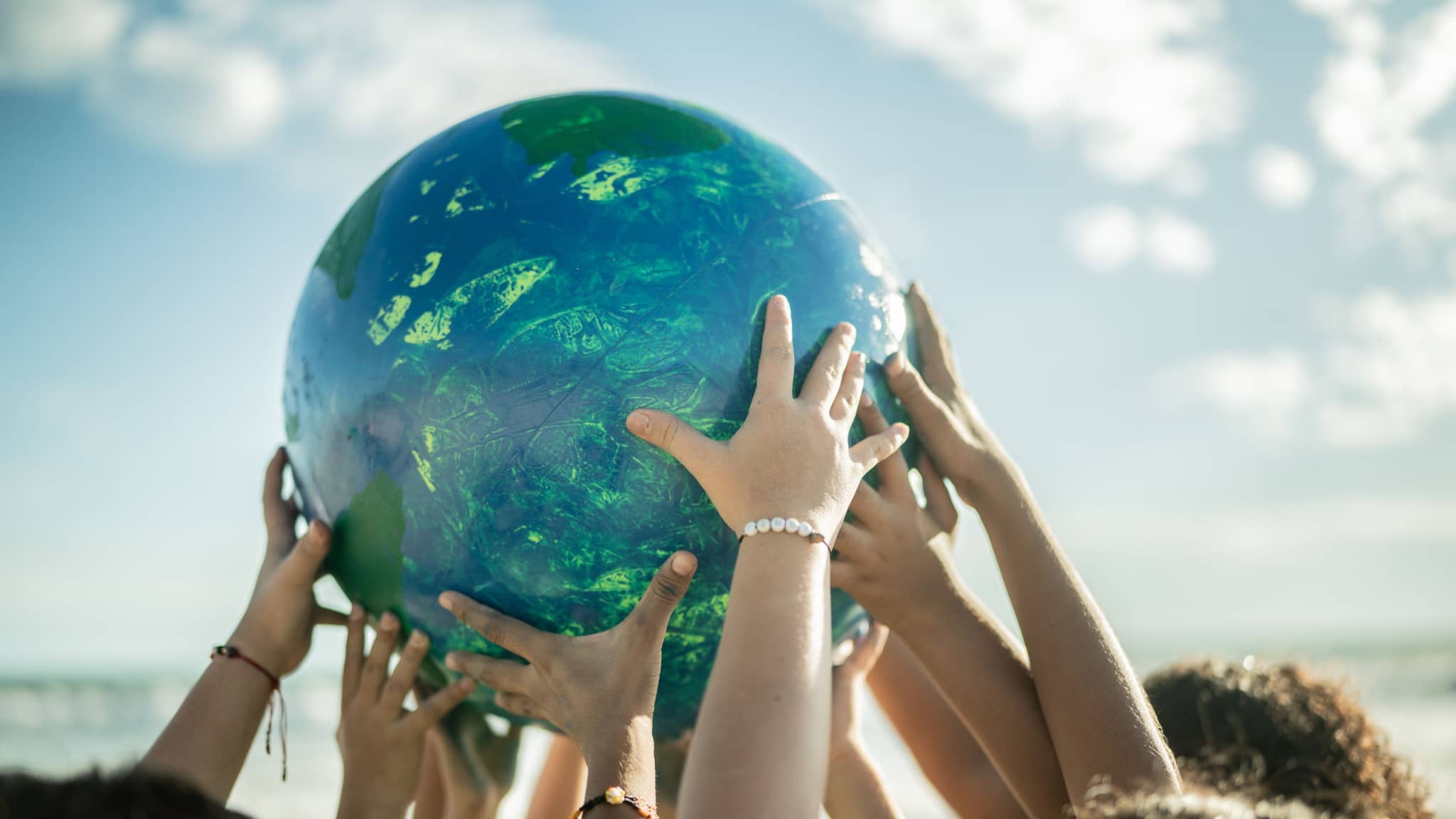 Nachhaltigkeit: Am Strand halten mehrere Kinder einen großen Ball nach oben, der an einen Planeten erinnert.