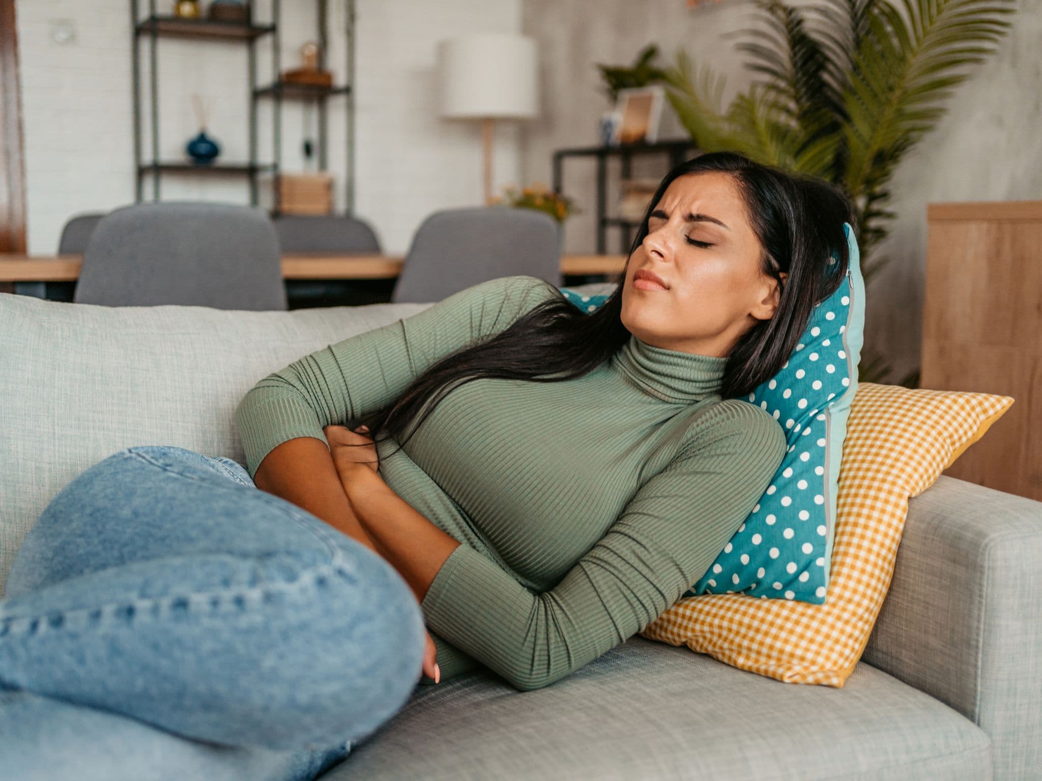 Zöliakie: Junge Frau liegt auf ihrem Sofa und verspürt Schmerzen im Bauch