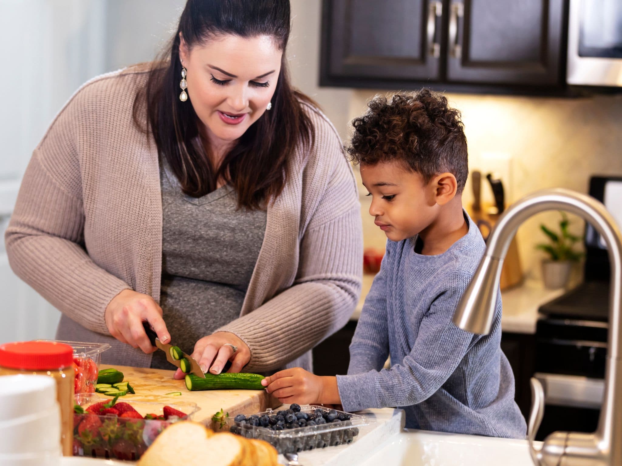 Gesund abnehmen: Eine Frau steht in der Küche und schneidet Gemüse, ein kleiner Junge schaut zu