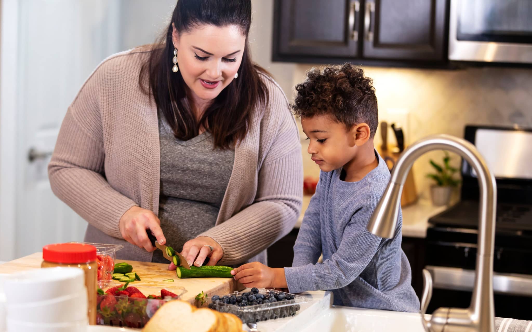 Gesund abnehmen: Eine Frau steht in der Küche und schneidet Gemüse, ein kleiner Junge schaut zu